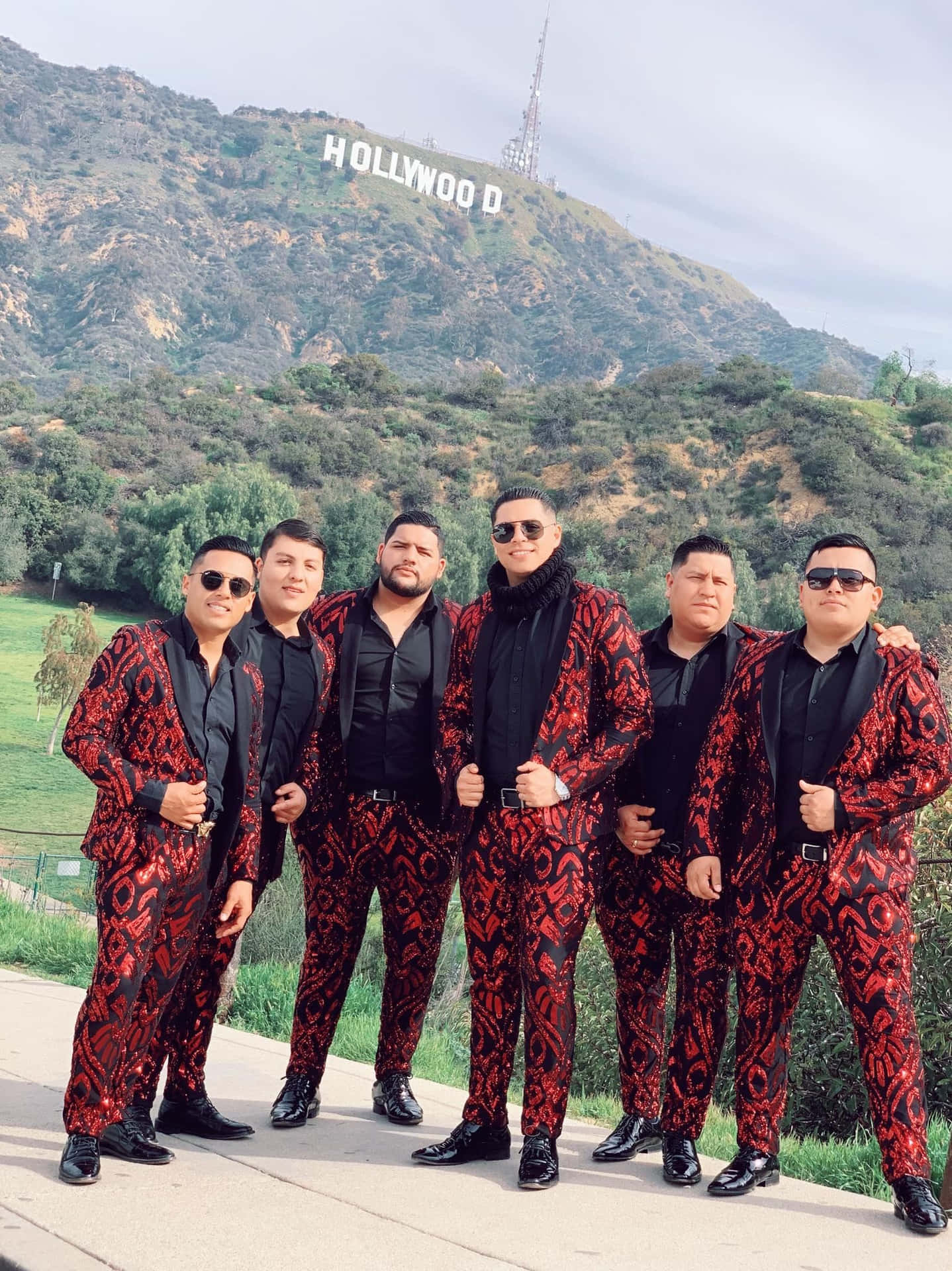 A Group Of Men In Suits Standing In Front Of The Hollywood Sign Wallpaper