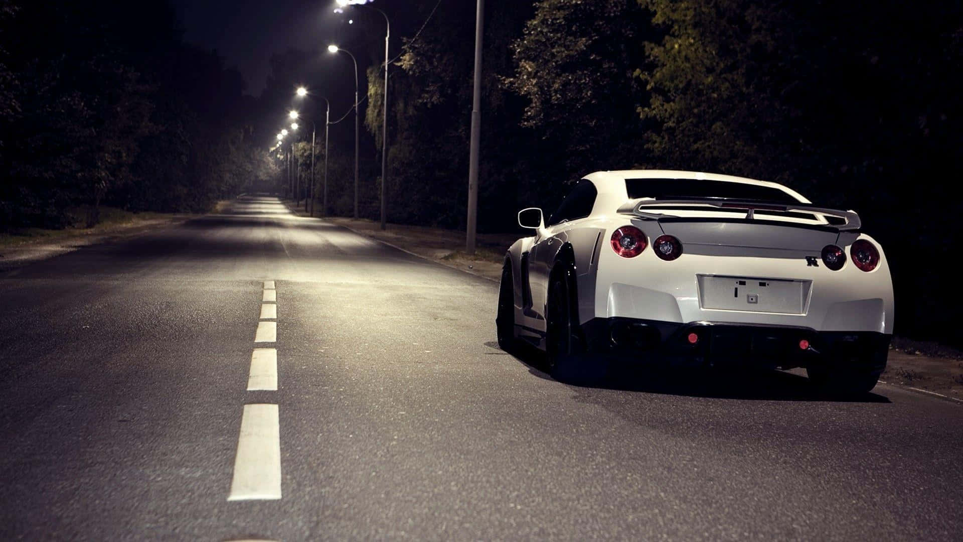 A White Sports Car Driving Down A Dark Road At Night Wallpaper