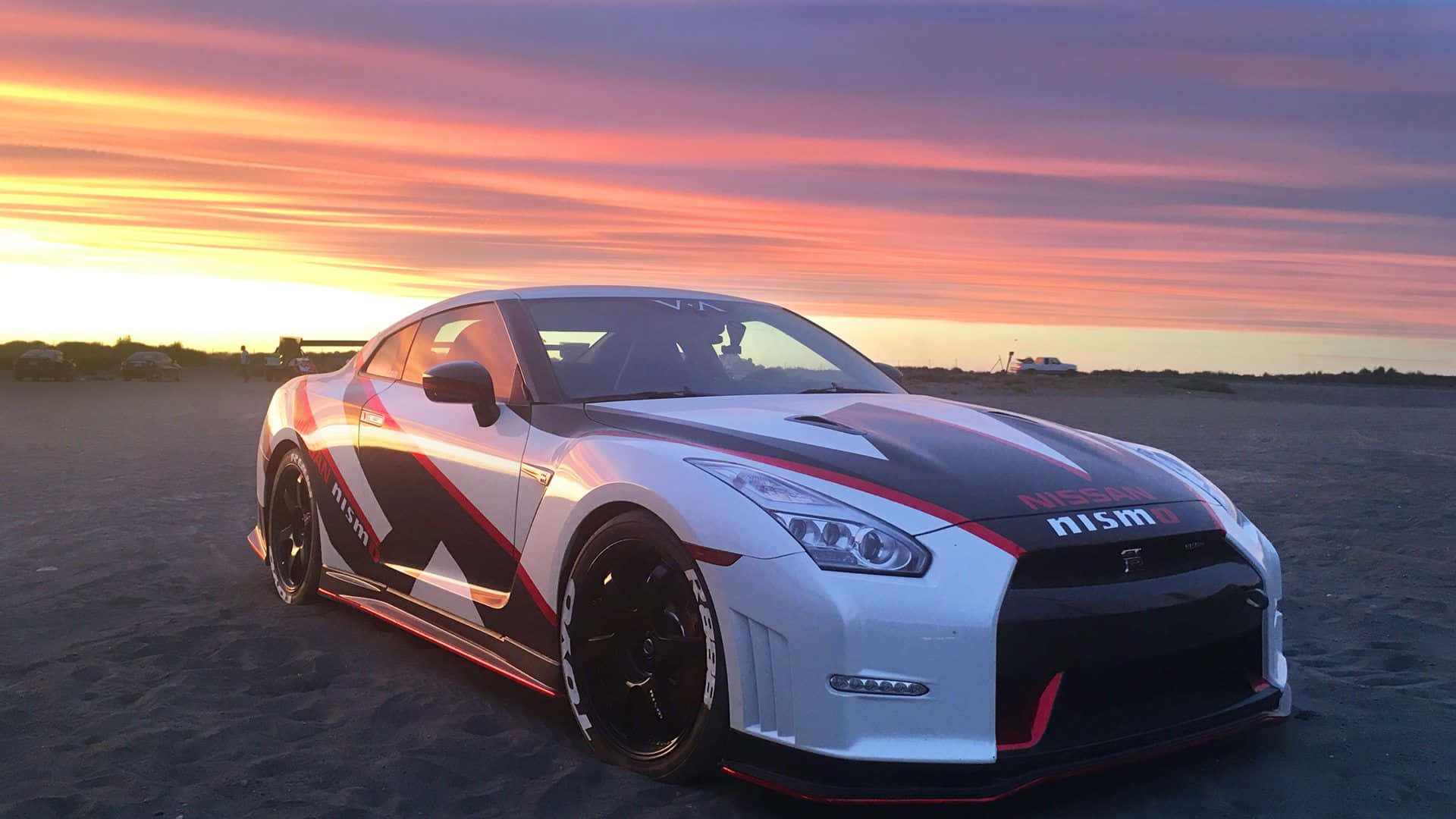 A Nissan Gtr Parked On The Beach At Sunset Wallpaper