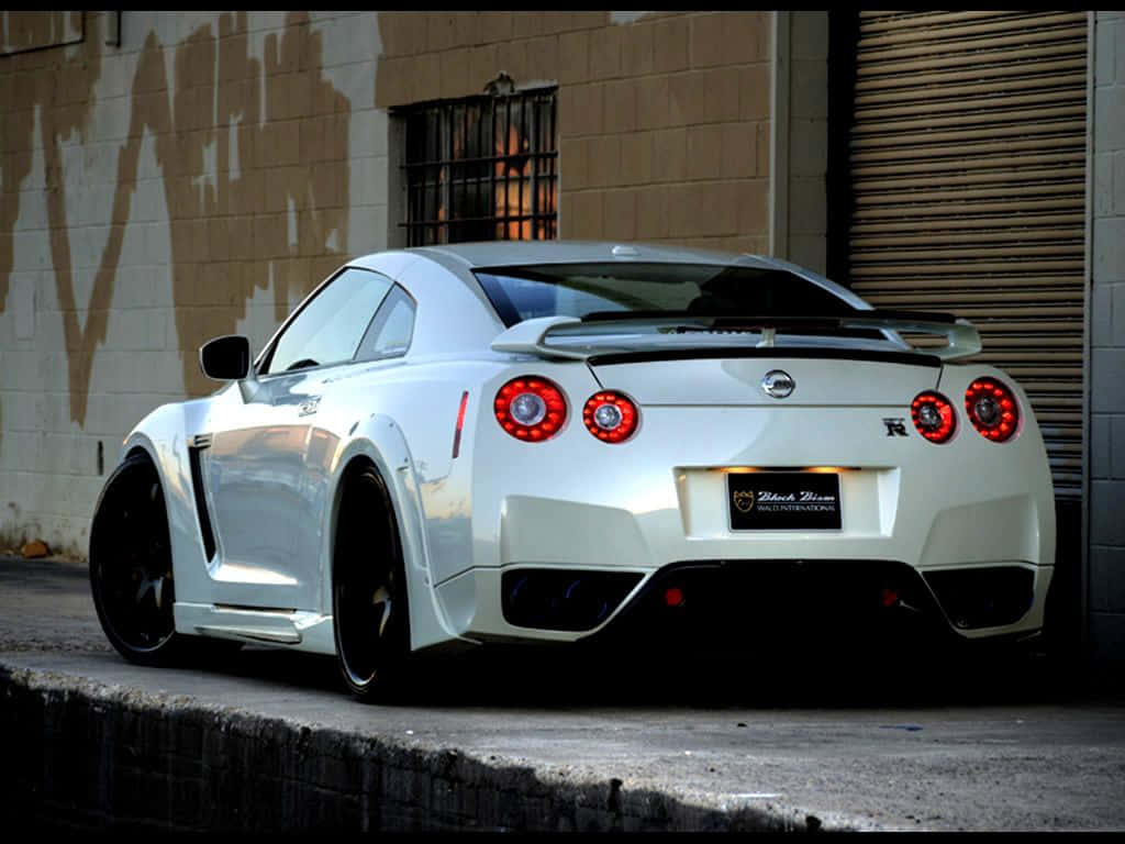 A White Nissan Gtr Parked In Front Of A Garage Wallpaper
