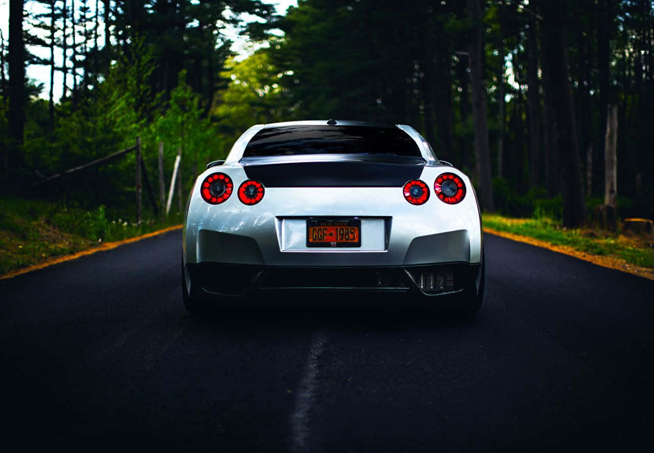 A White Sports Car Driving Down A Road In The Woods Wallpaper