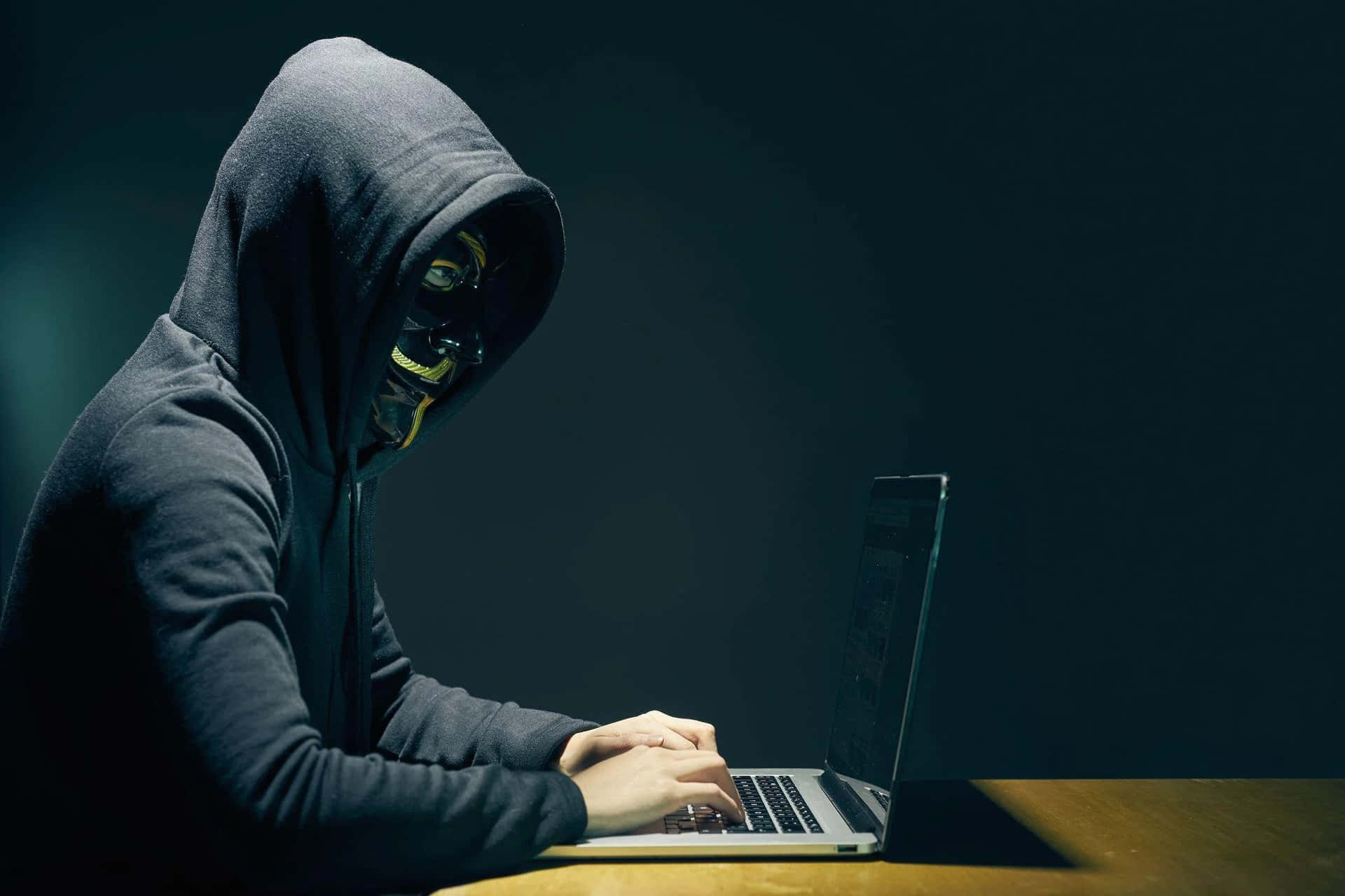 A Man In A Hoodie Is Using A Laptop