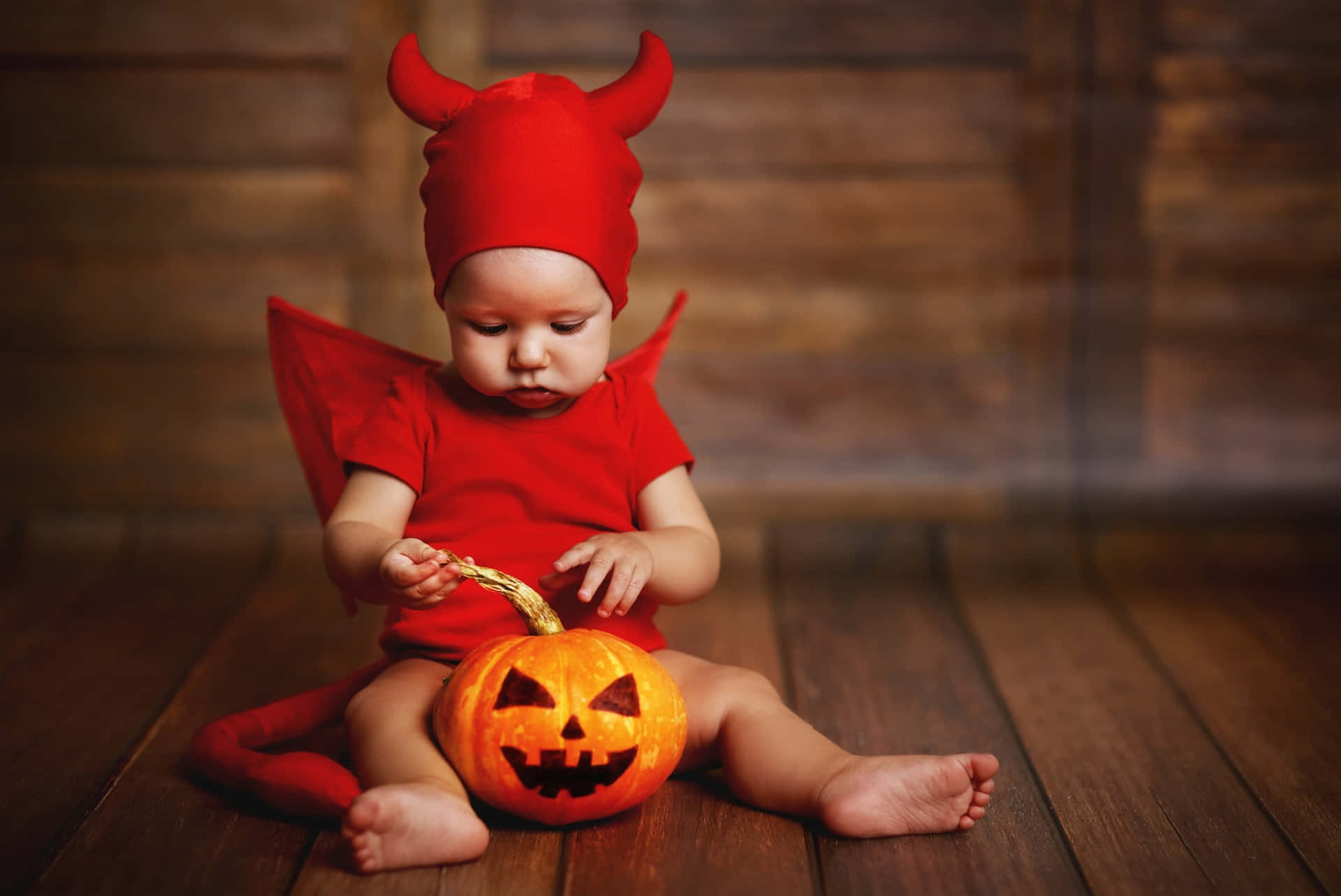 A Baby Dressed As A Devil With A Pumpkin