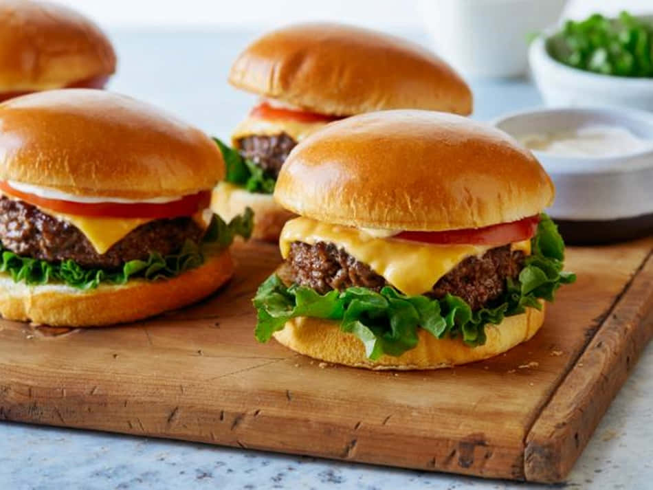 Four Cheeseburgers On A Wooden Cutting Board