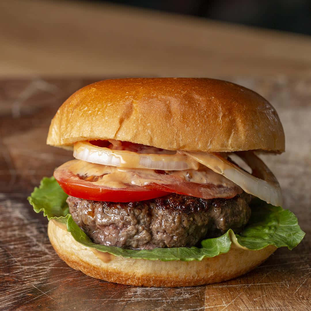 A Burger With Lettuce, Tomato And Onion On A Wooden Board