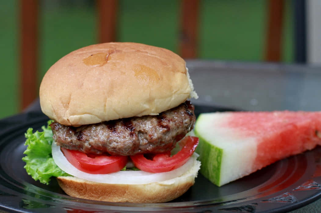 A Hamburger With Lettuce, Tomatoes And Watermelon On A Plate