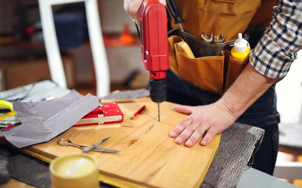 A Man Is Working On A Wooden Board With A Drill
