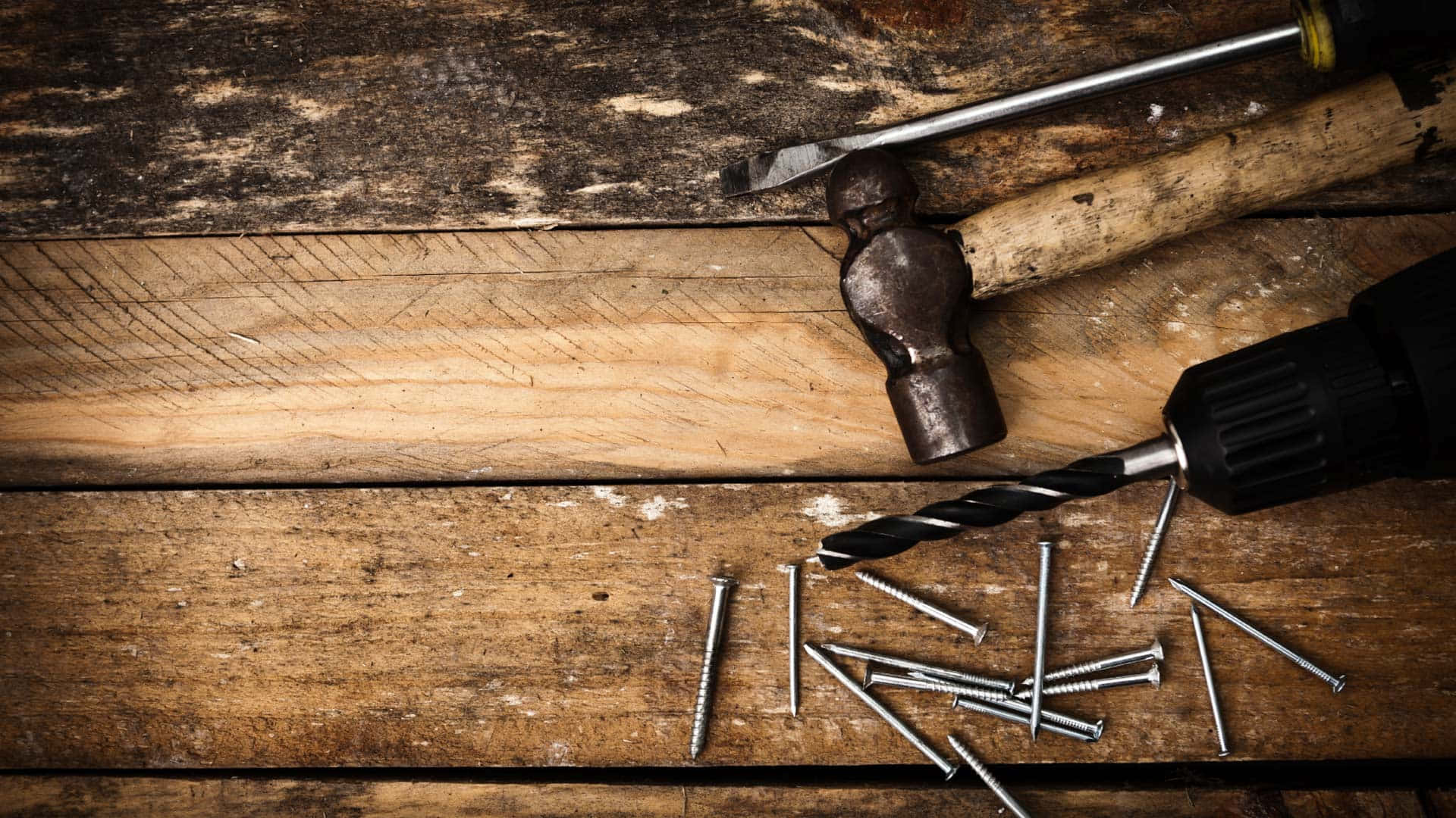 A Drill, Screwdriver, And Nails On A Wooden Table