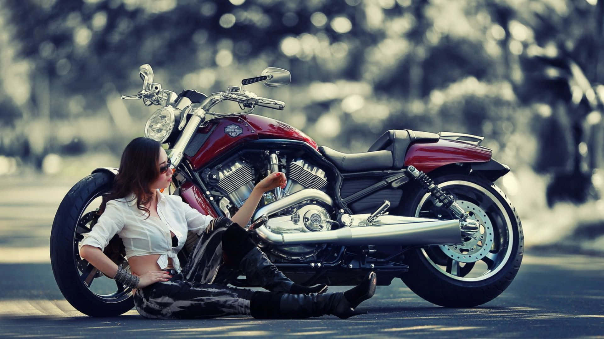 En kvinde sidder på jorden ved siden af ​​en motorcykel Wallpaper