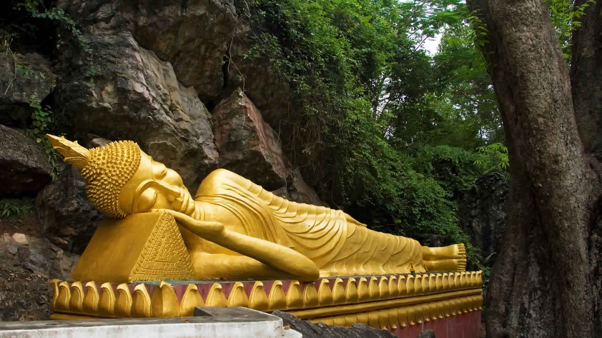a golden buddha statue is laying down in a cave Wallpaper