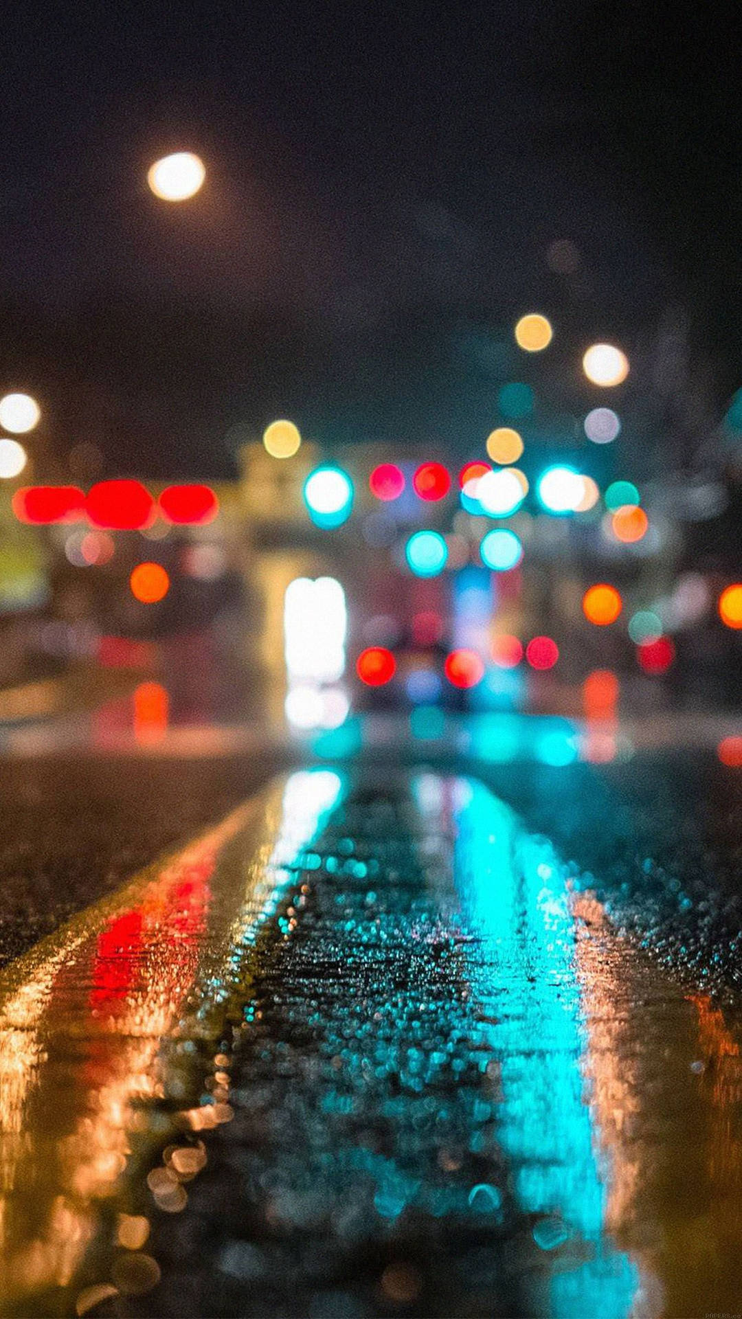 HD wallpaper of wet road and blurry city lights at night.