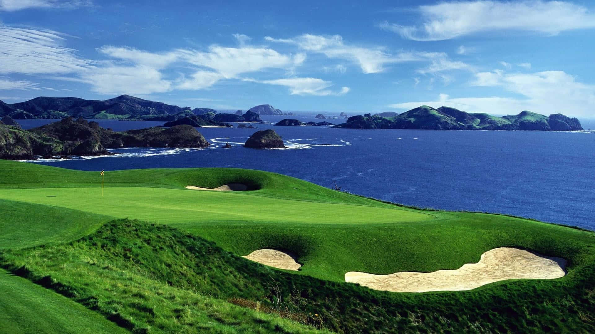 En golfbane med en grøn bunker og havet ude i horisonten.