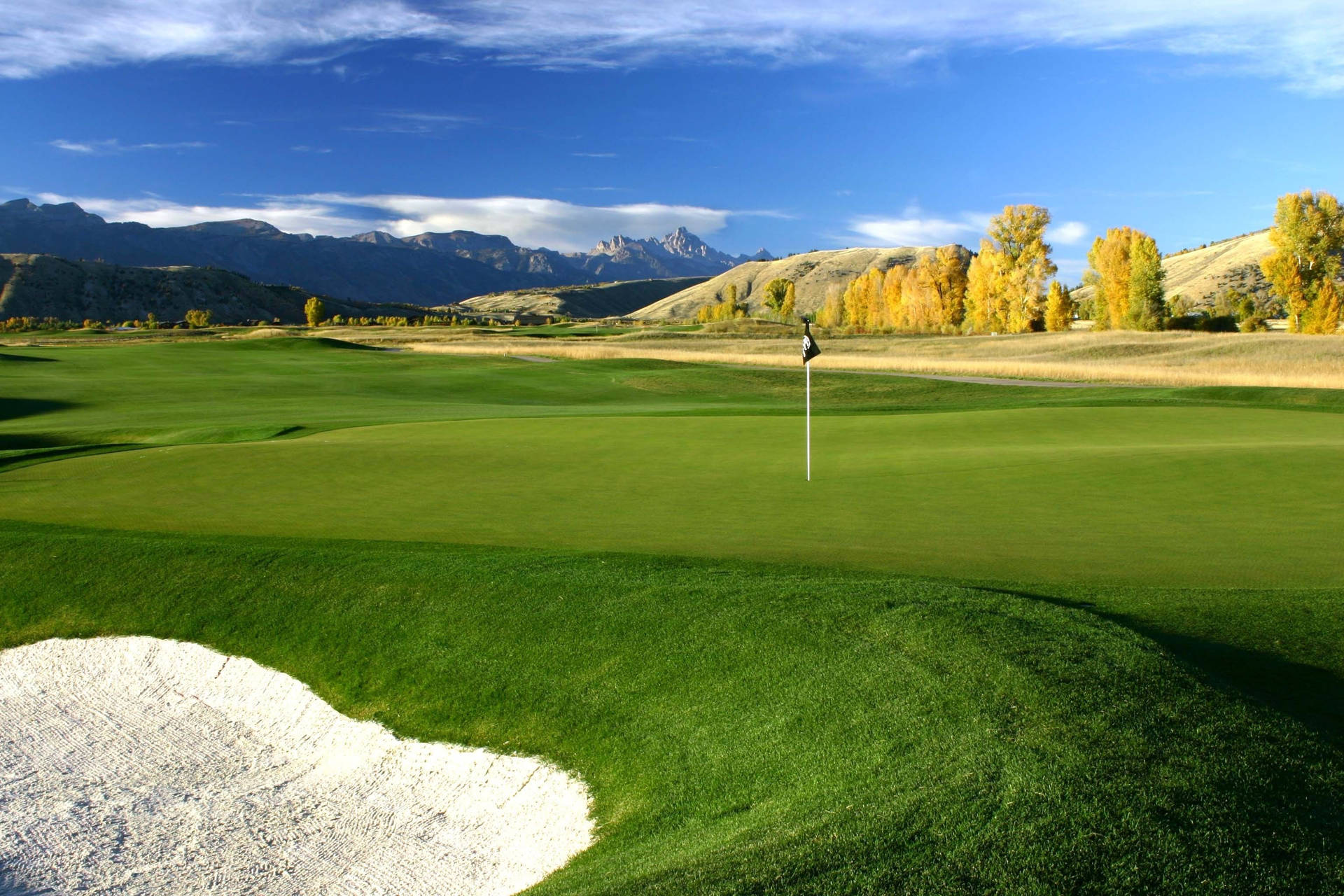 A Green Golf Course With Mountains In The Background Wallpaper