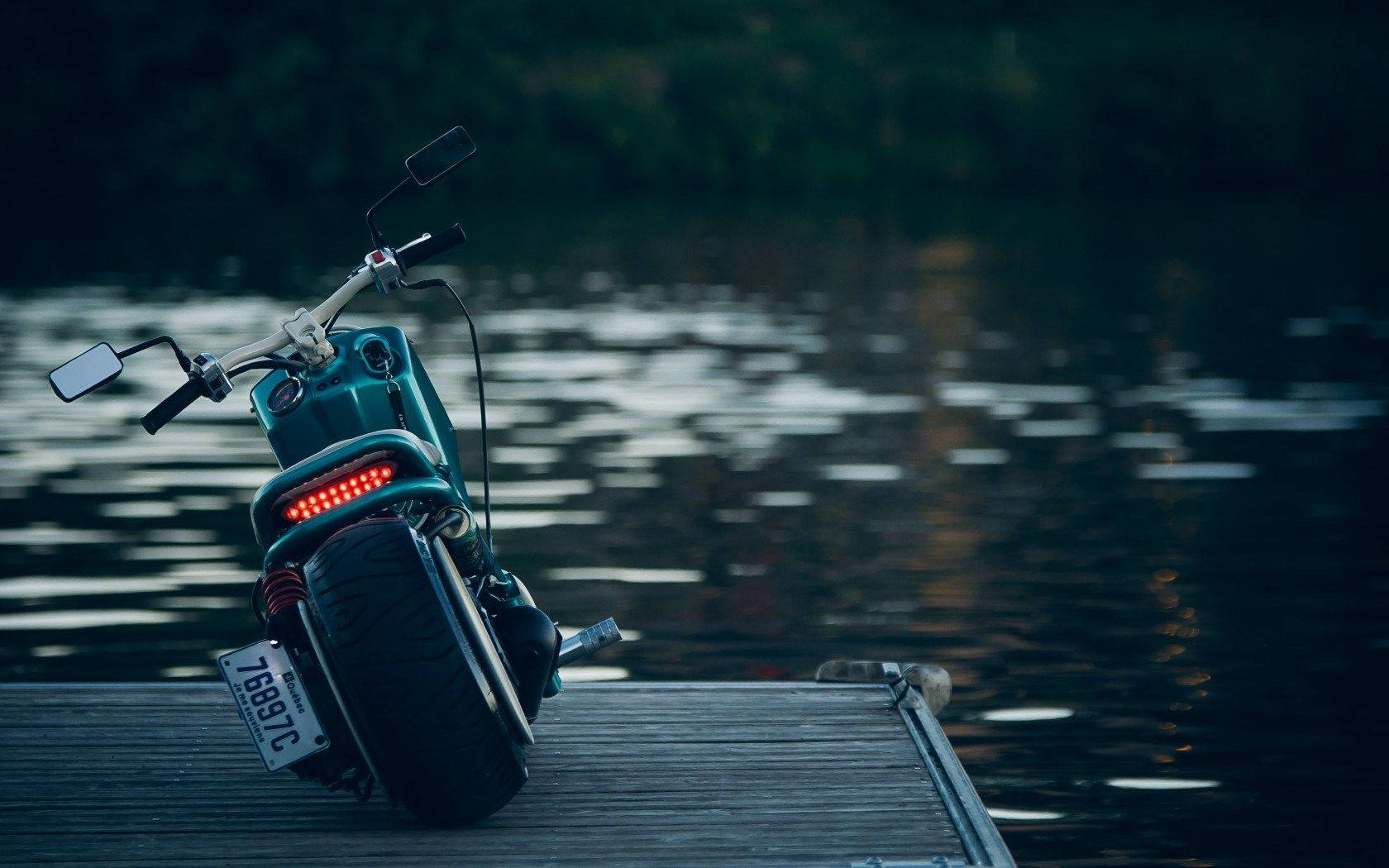 Intrepid explorer riding on a motorcycle near a pristine alpine lake Wallpaper