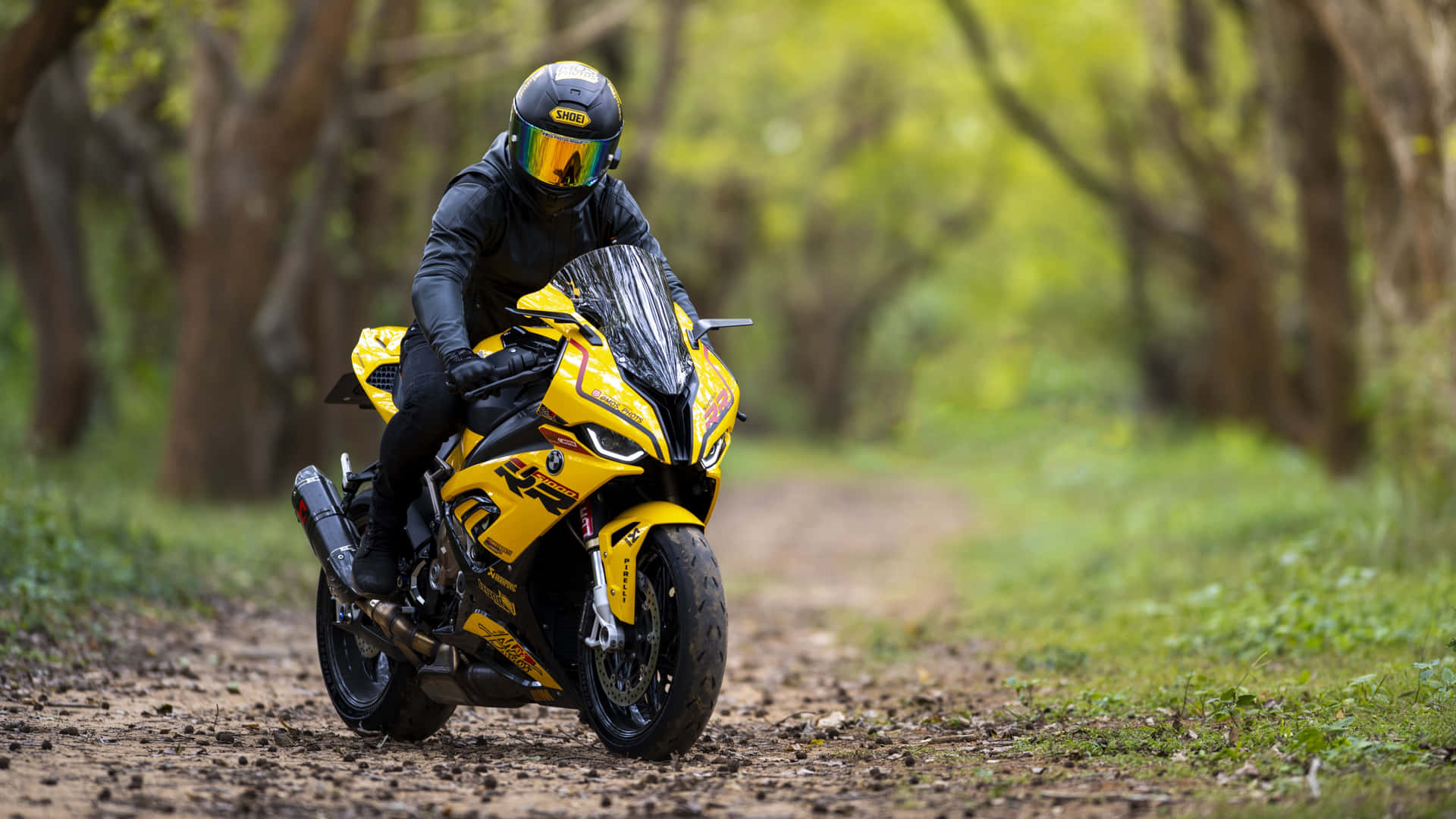 En person kører en gul motorcykel på en skovvej. Wallpaper
