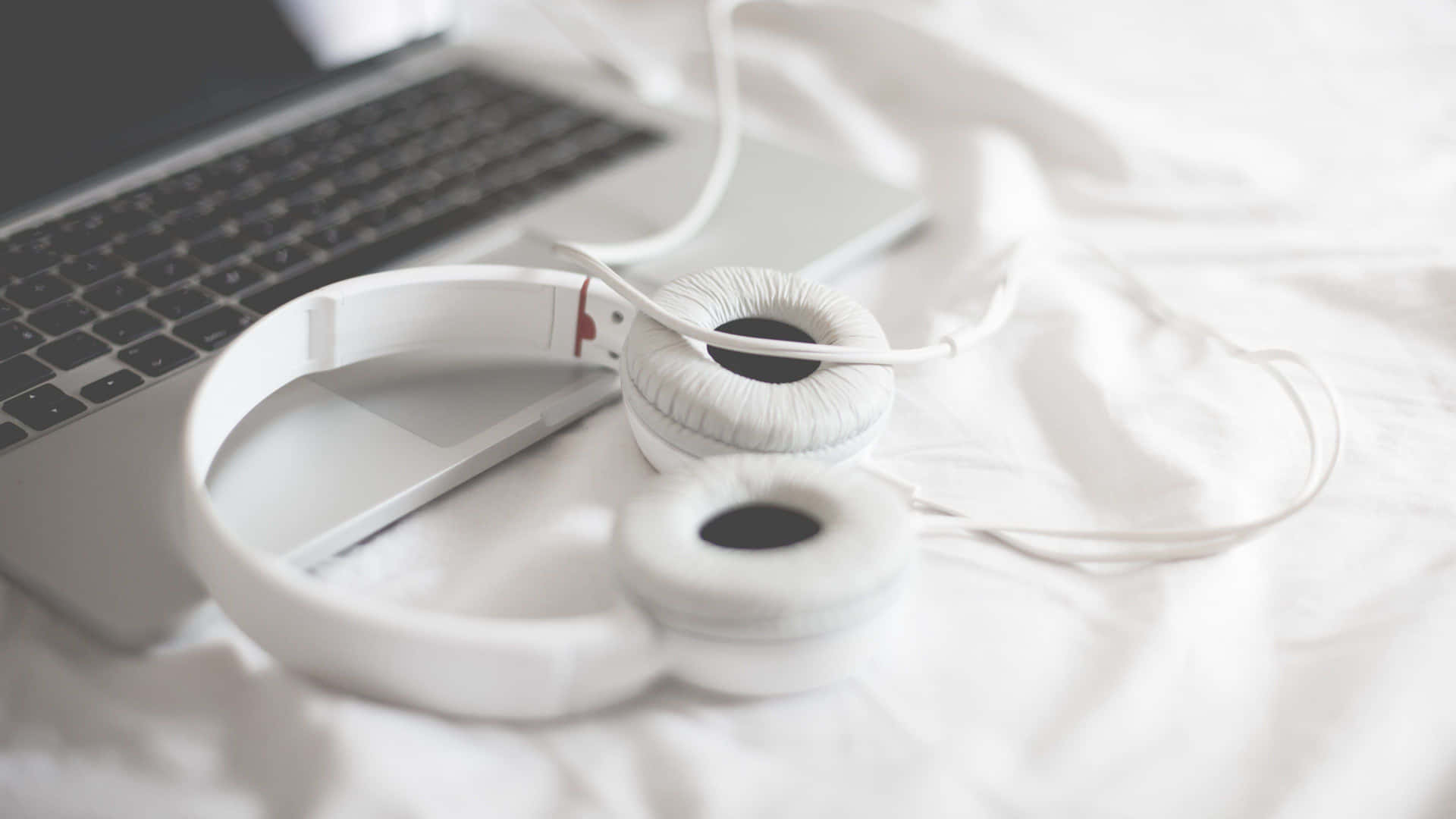 White Headphones On A Bed Next To A Laptop Wallpaper