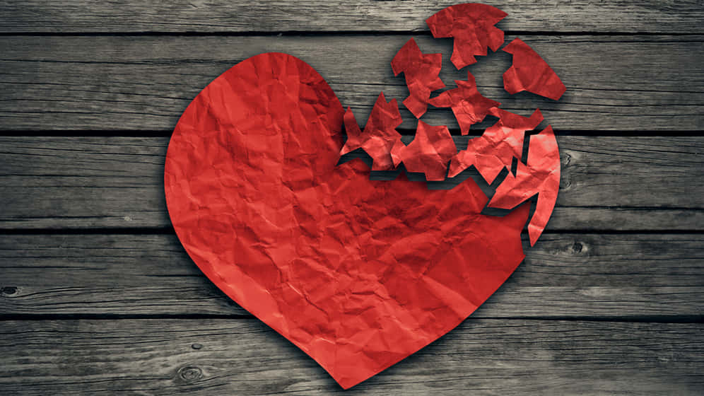 a red heart with a broken piece of paper on a wooden background