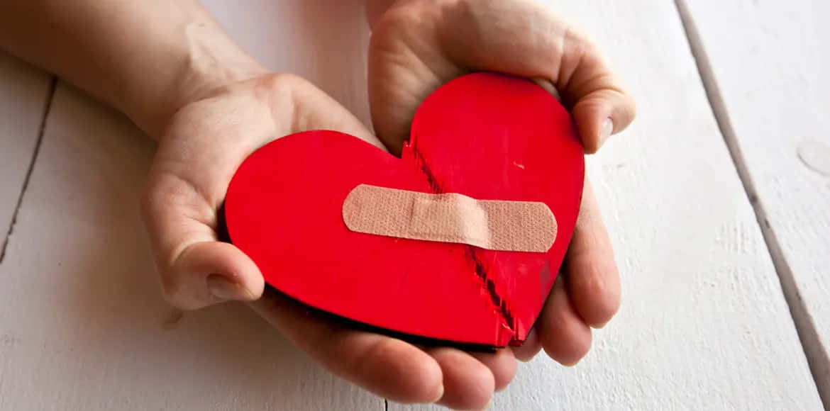 En person der holder et rødt hjerte med et bandage på det.
