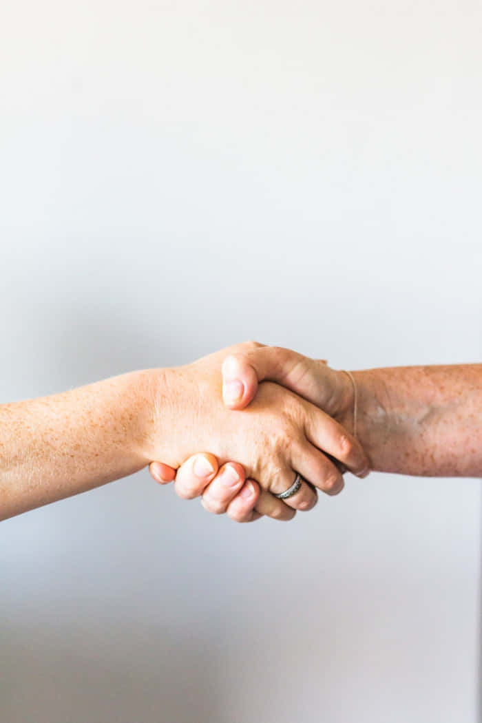 Two People Shaking Hands In Front Of A White Background