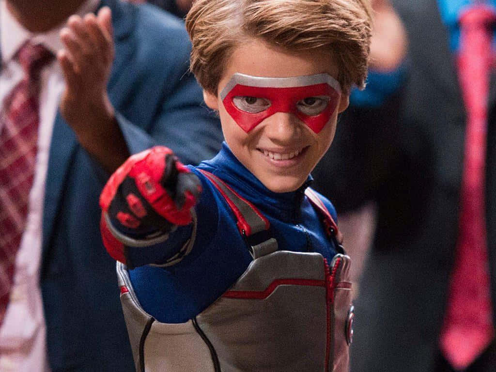 En ung dreng i en superhelt kostume peger mod menneskemængden. Wallpaper