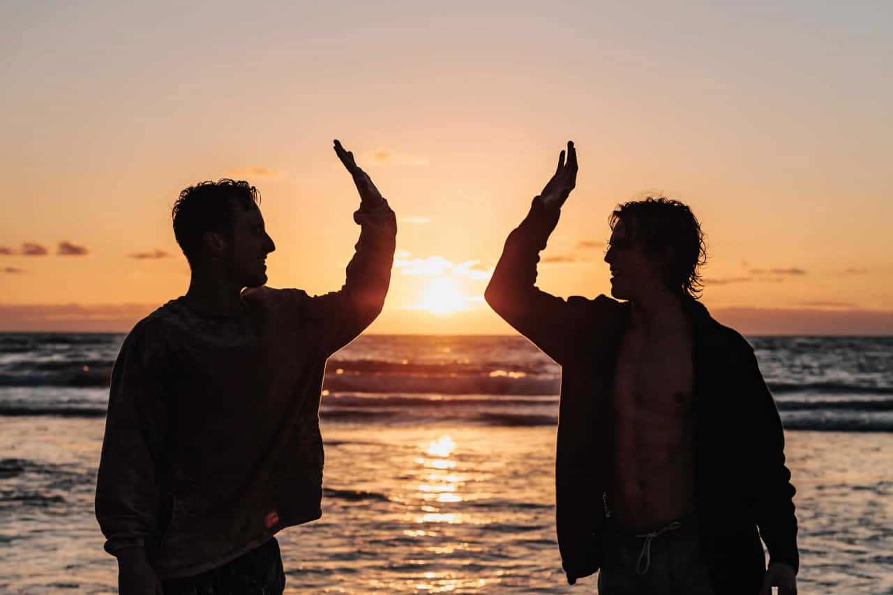 Two Men Standing On The Beach At Sunset