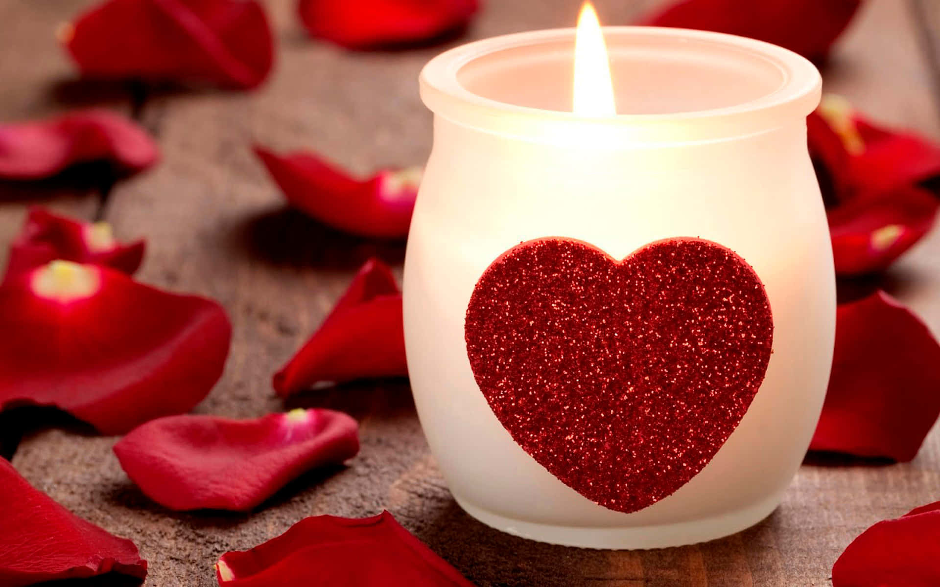 A Candle With Red Hearts On It Sits On Top Of Rose Petals