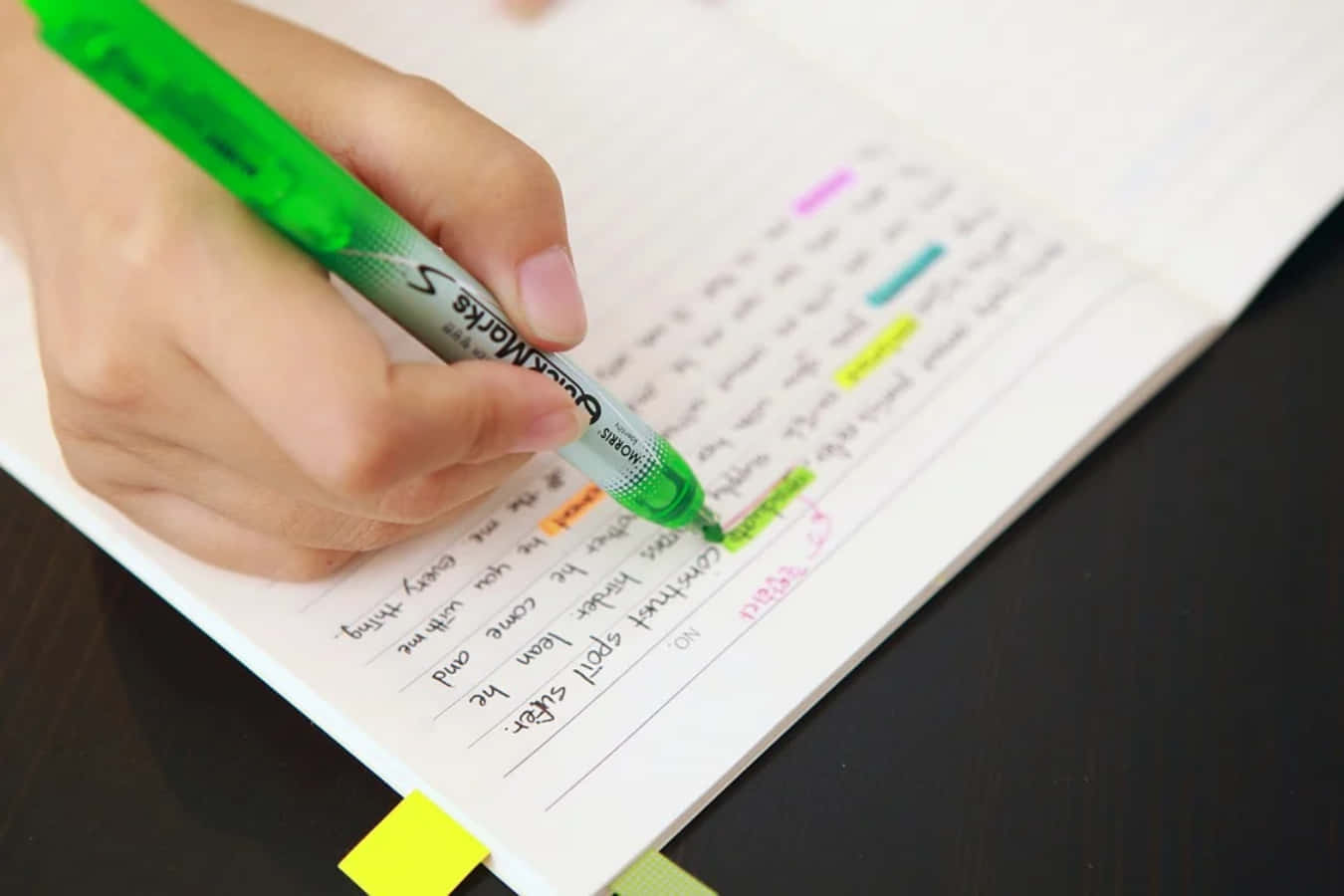 A Person Writing In A Notebook With A Green Pen