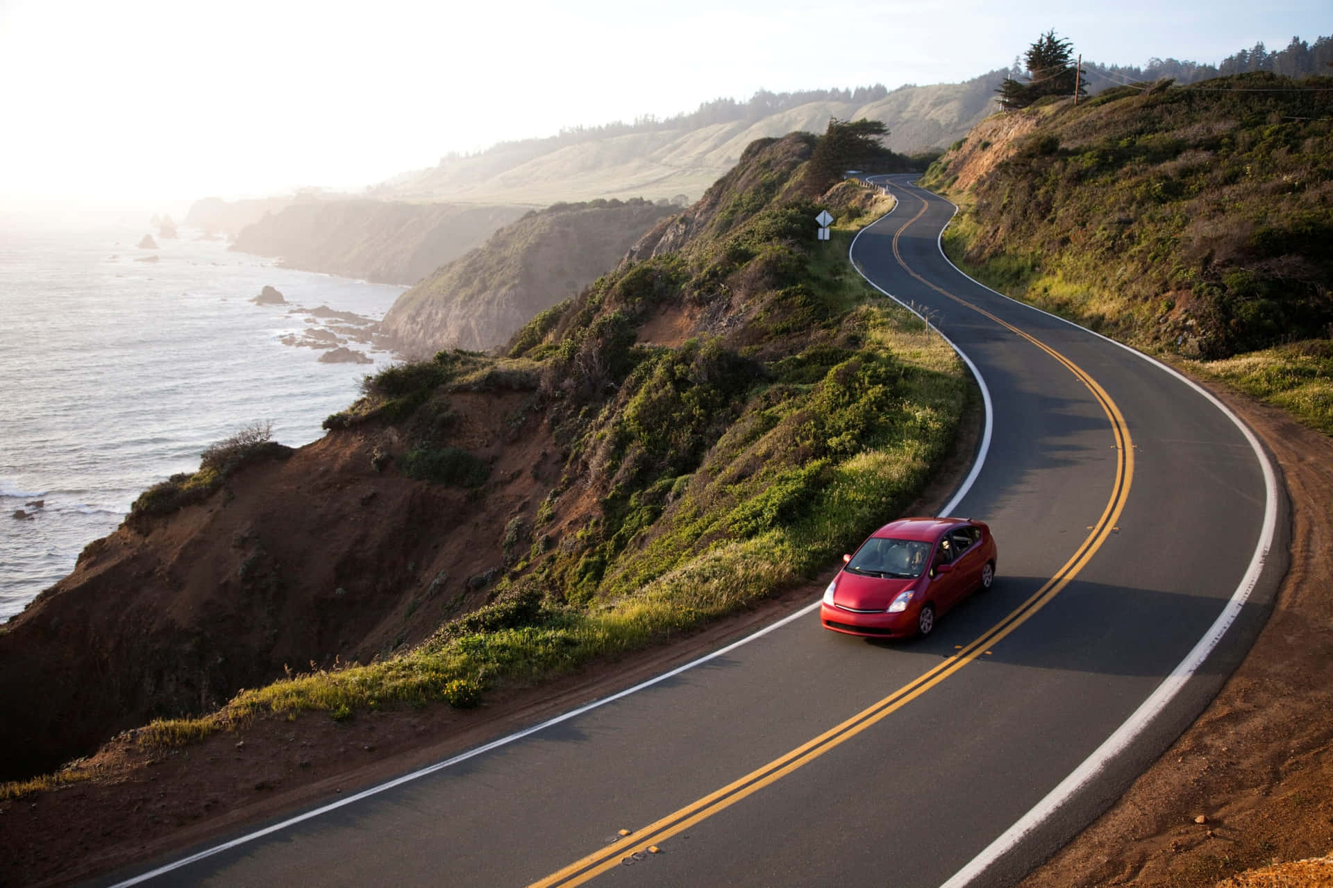A Red Car Driving Down A Winding Road Near The Ocean