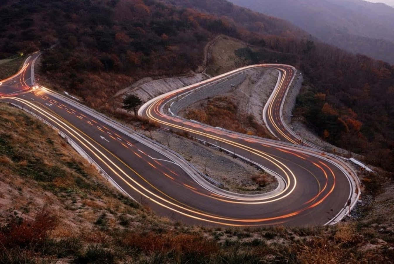A Winding Road With Light Trails In The Mountains