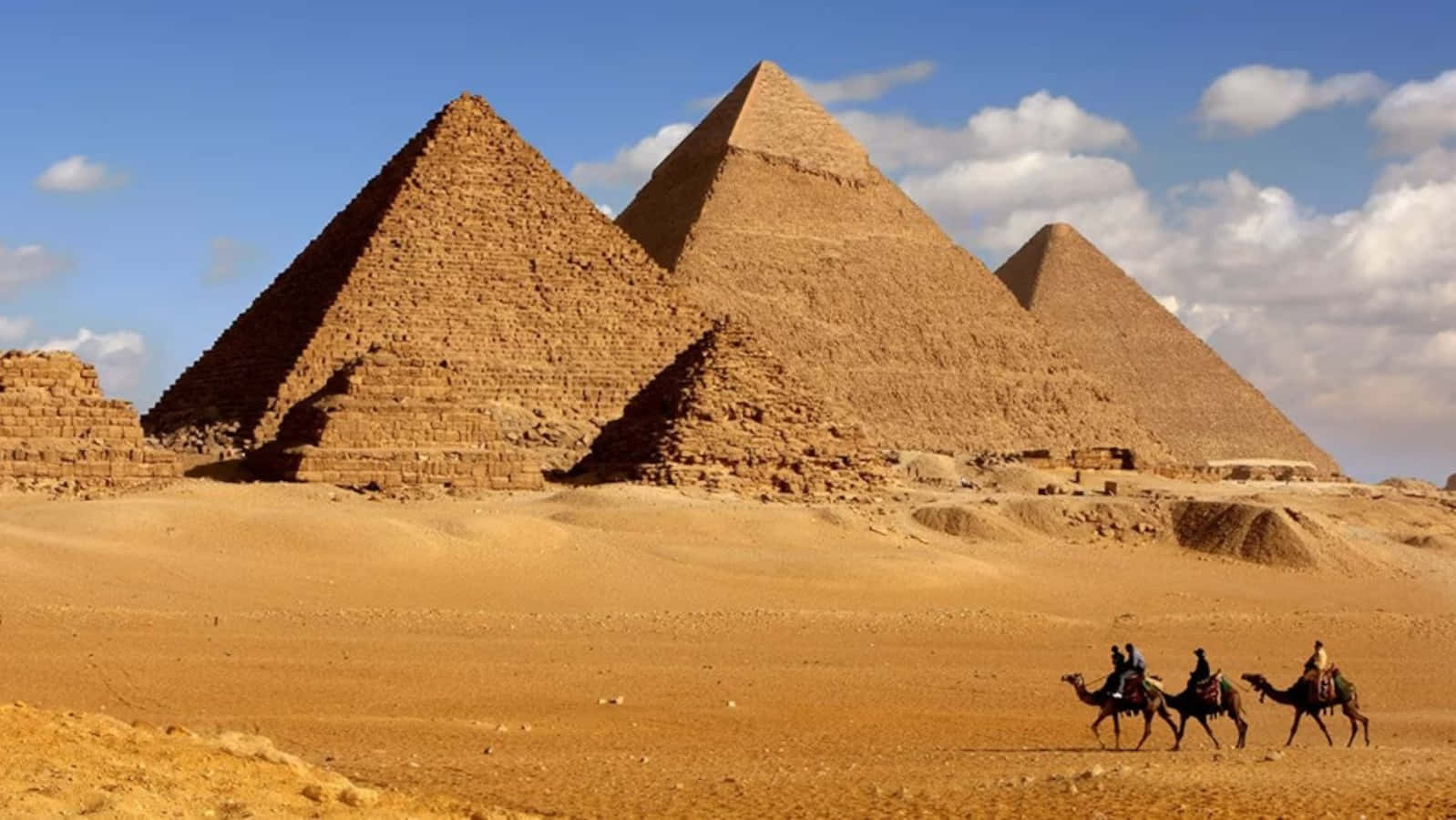 Three People Riding Camels In Front Of The Pyramids