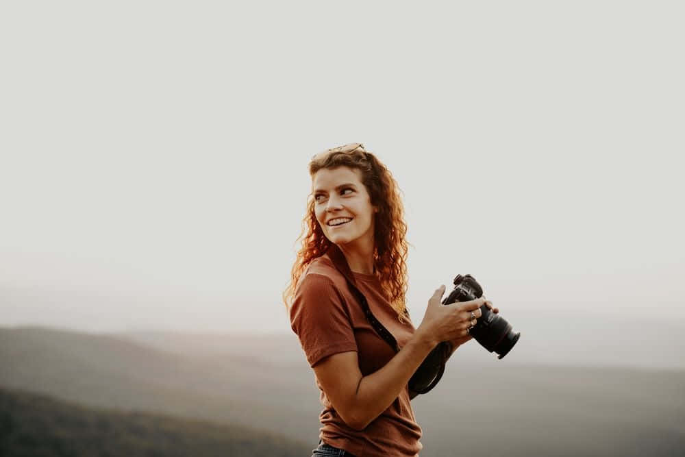 A Woman Holding A Camera In The Mountains