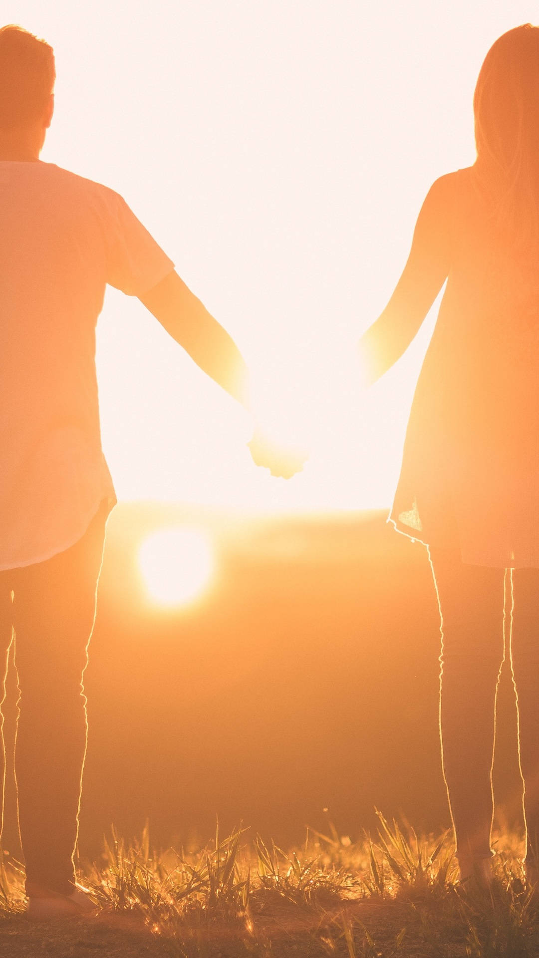 Paar,das Hände Haltend Den Sonnenuntergang Entgegenblickt - Aufnahme Von Hinten Wallpaper