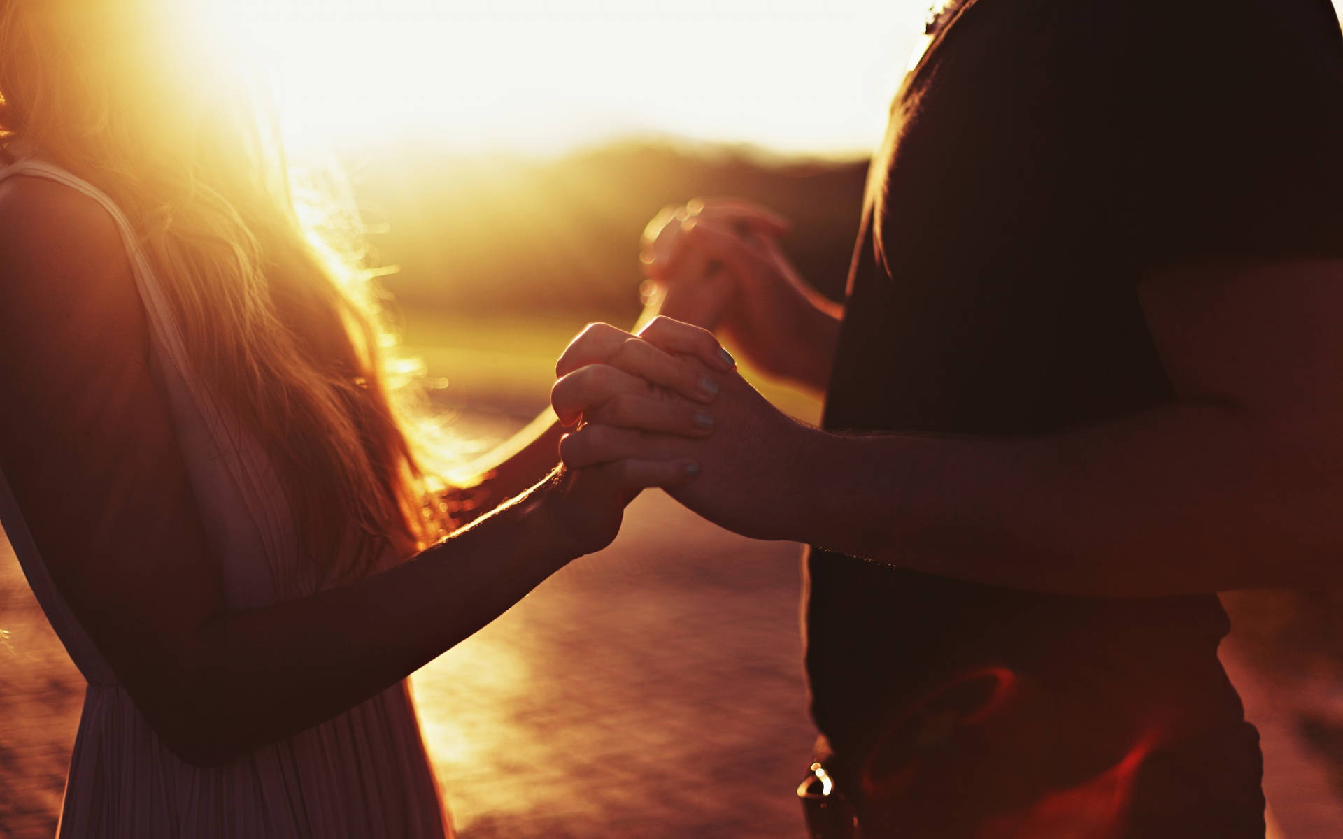 Holding Hands While Facing Each Other At Sunset Wallpaper