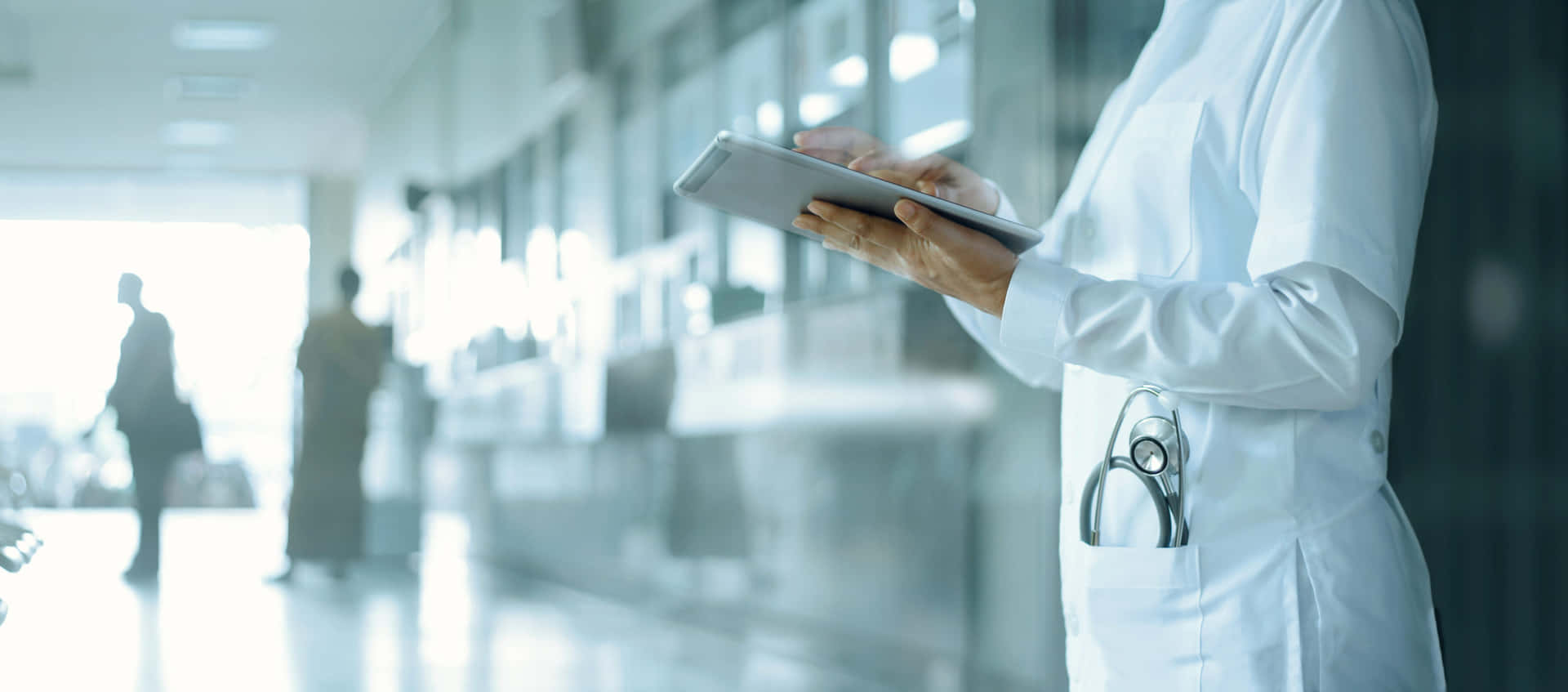 A Nurse Is Holding A Tablet In A Hallway