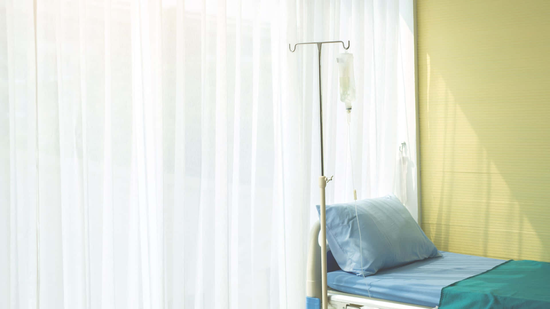 A Hospital Bed With A Blue Blanket And Yellow Curtains
