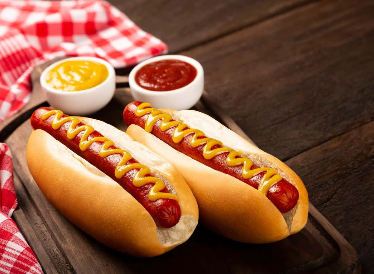 Two Hot Dogs With Mustard And Ketchup On A Wooden Board