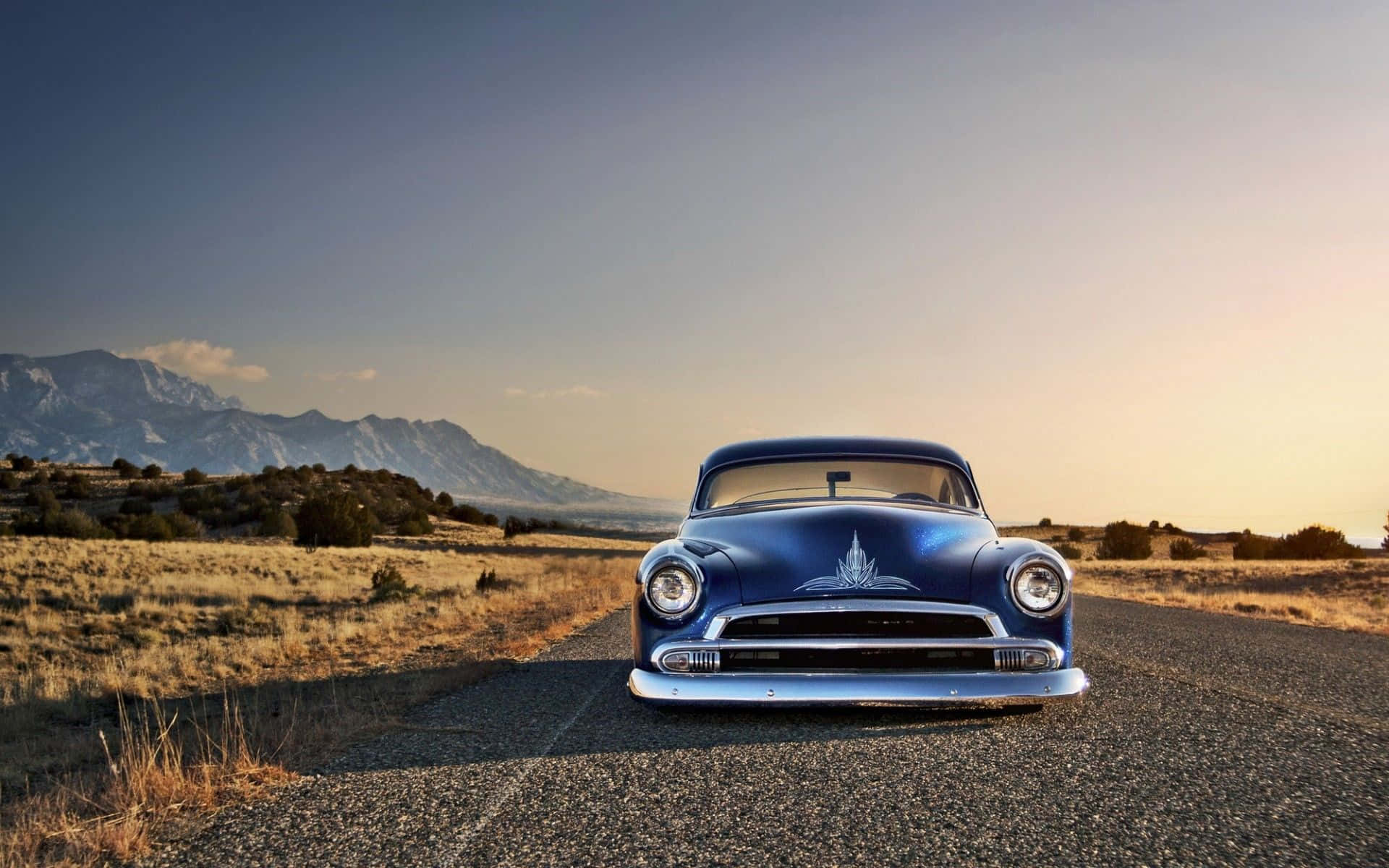 A Blue Classic Car Is Parked On A Road In The Mountains Wallpaper