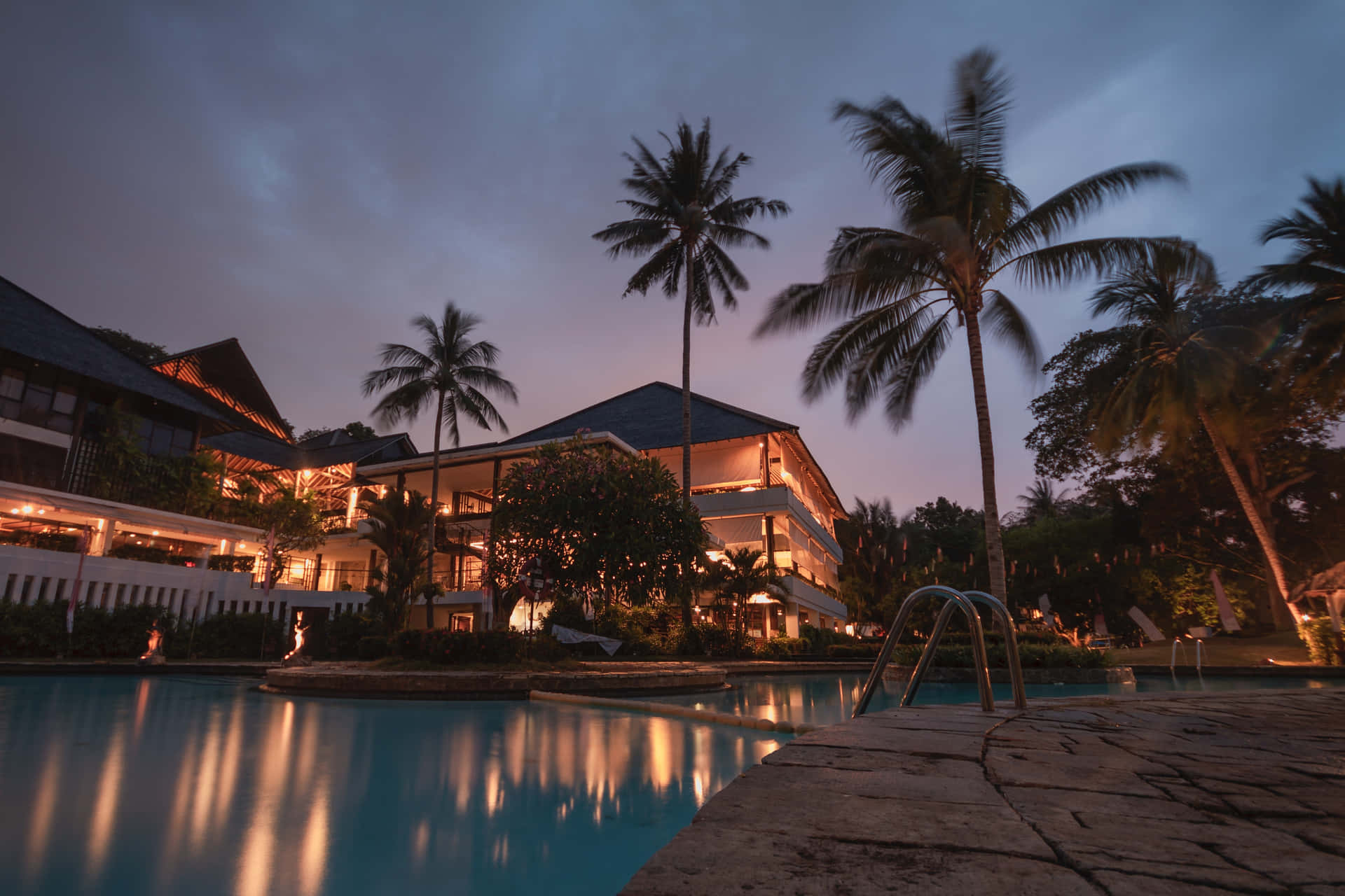 A Resort With A Pool And Palm Trees At Night