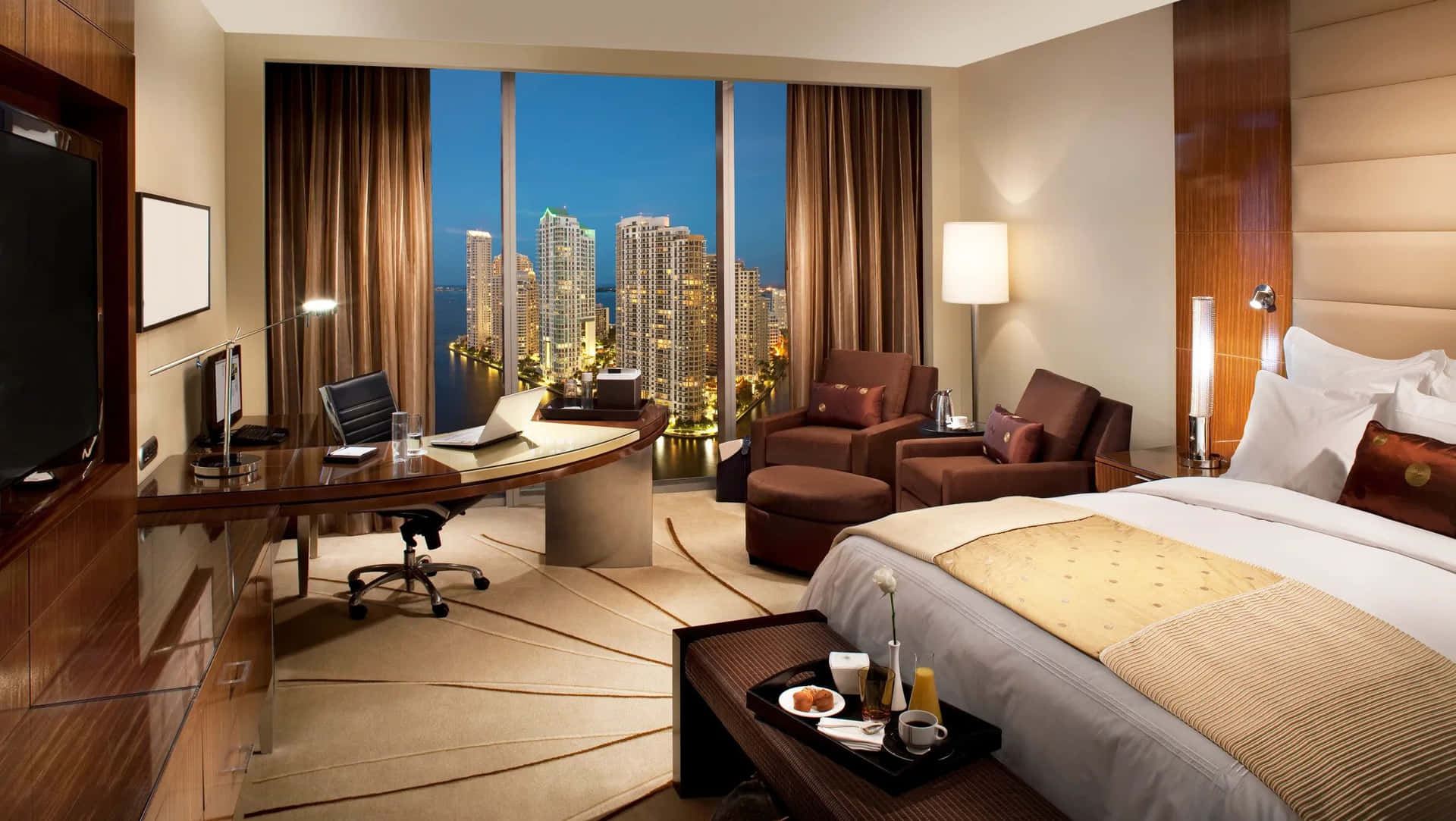 A Hotel Room With A Bed, Desk, And A View Of The City