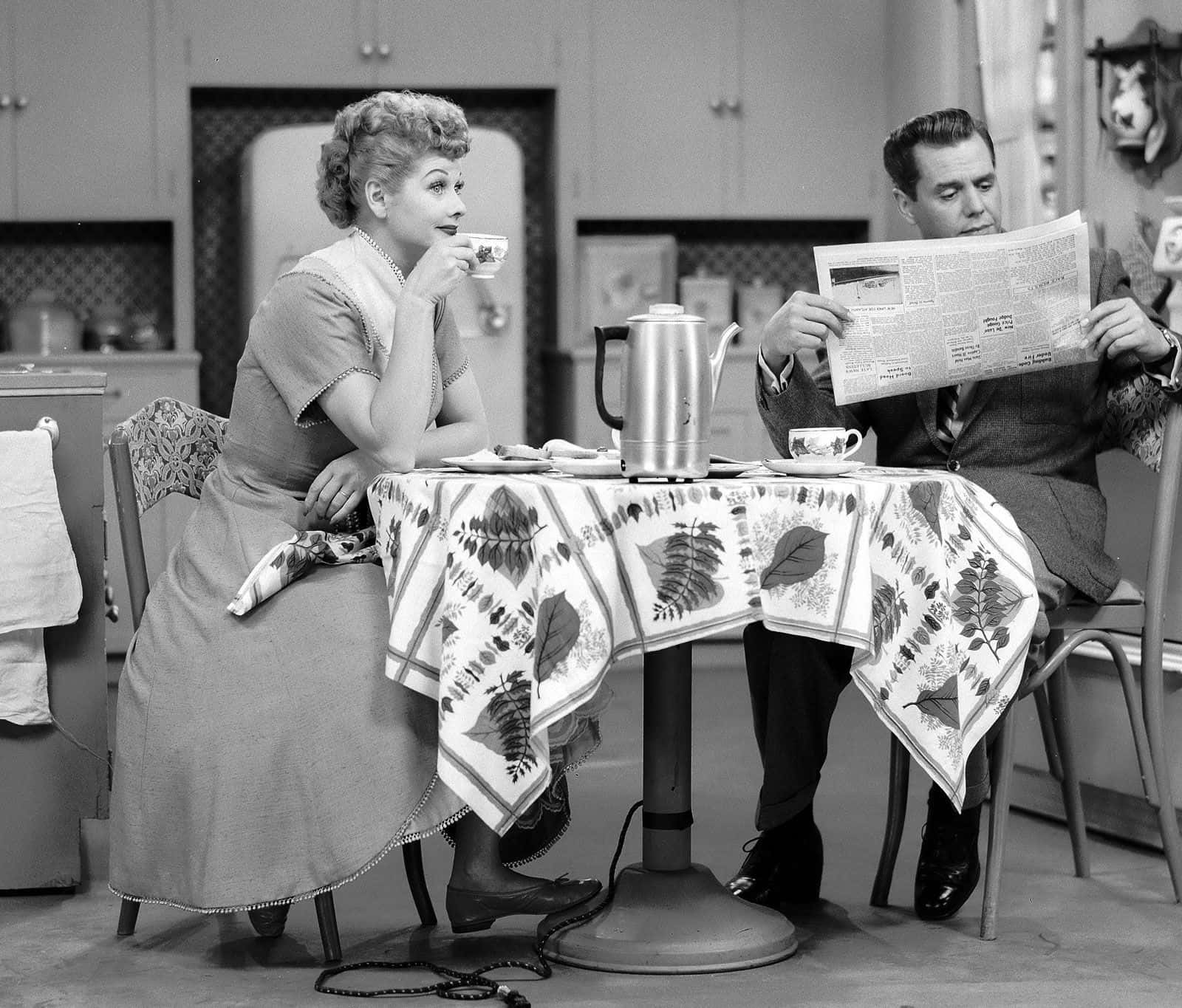 A Man And Woman Sitting At A Table Reading A Newspaper Wallpaper