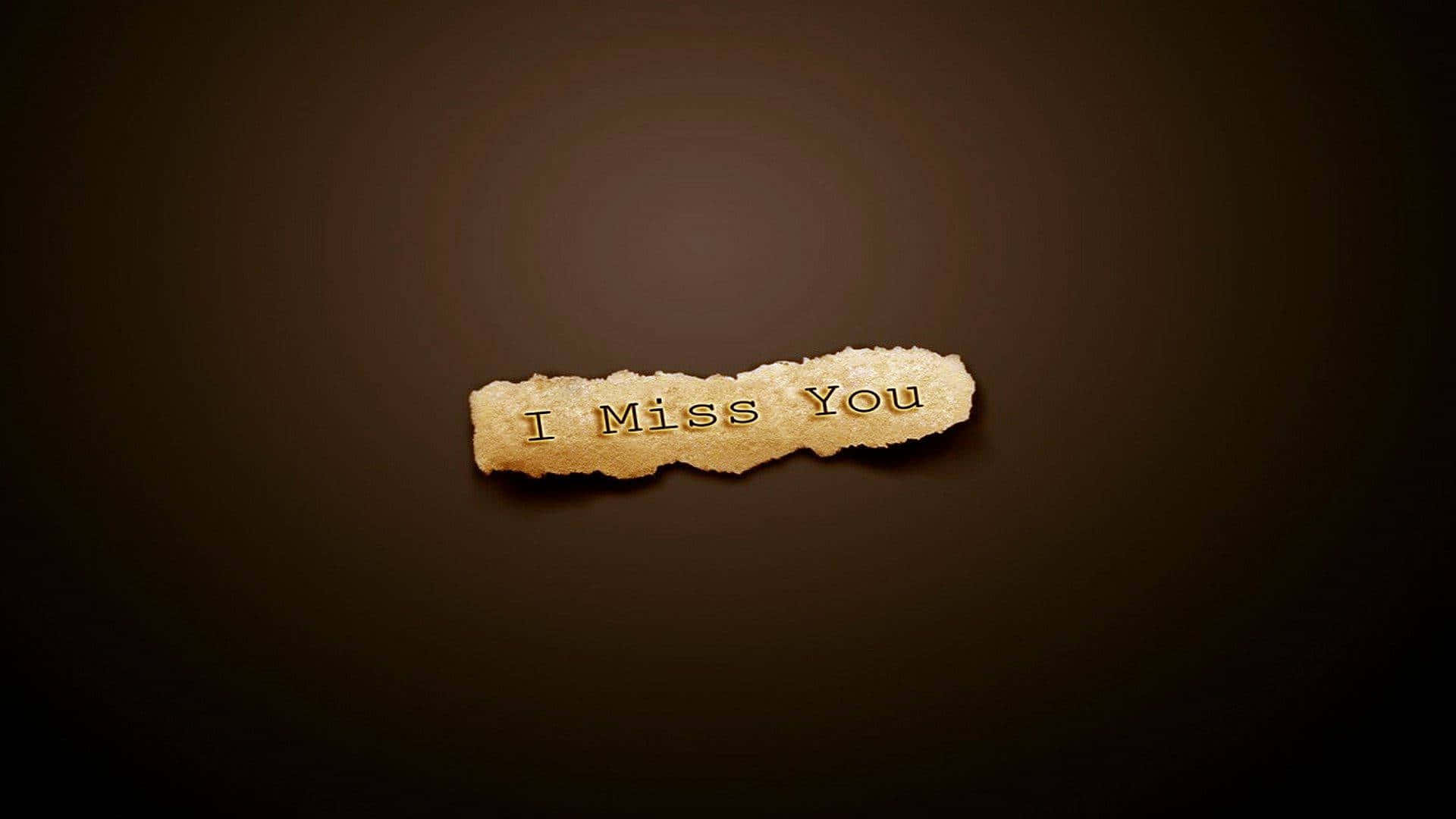 A heartfelt "I Miss You" written on a sandy beach with a setting sun in the background
