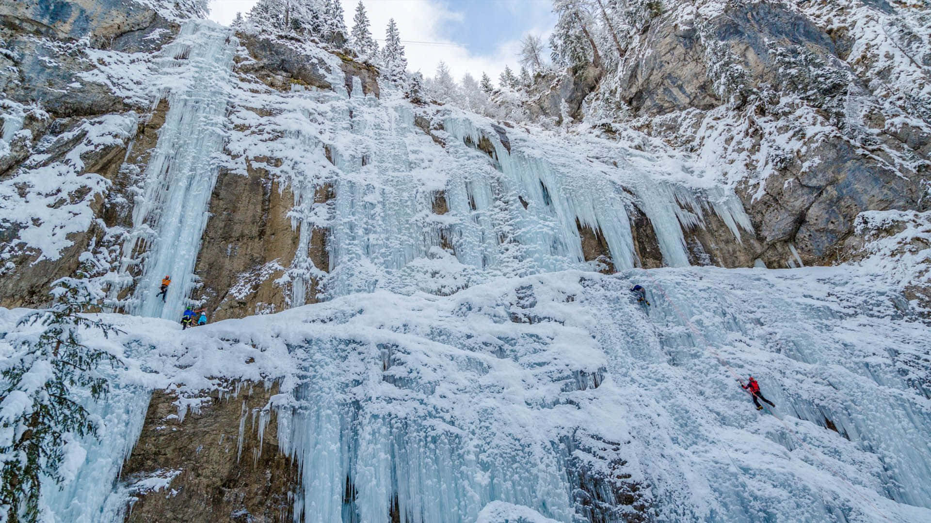Caption: Ice Climber Scaling a Frozen Waterfall Wallpaper