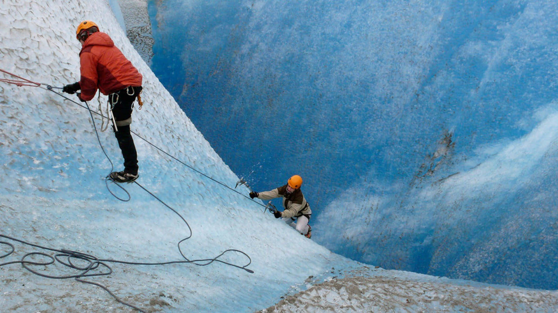 Fearless Ice Climber Ascending a Frozen Waterfall Wallpaper