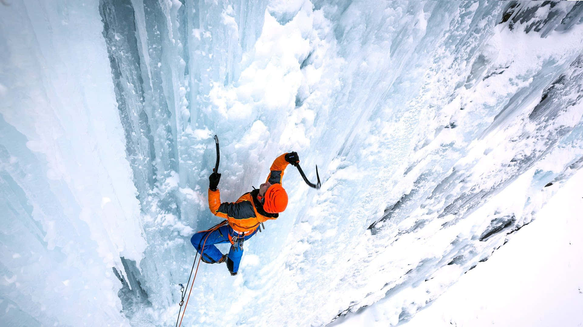 Fearless ice climber ascending a frozen waterfall Wallpaper