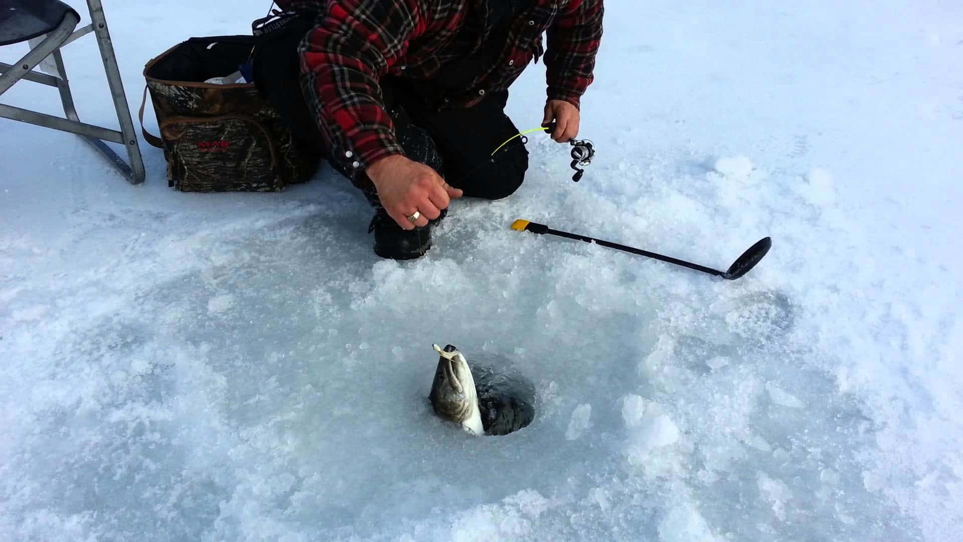 A fisherman enjoys a peaceful ice fishing session on a frozen lake Wallpaper