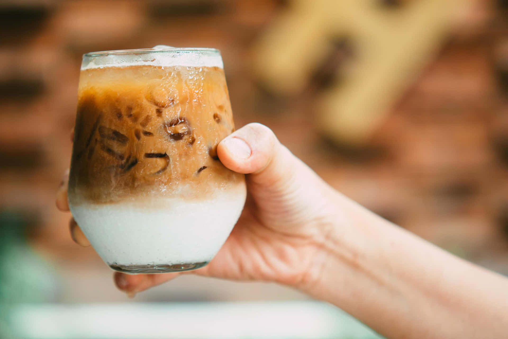 A Person Holding Up A Glass Of Iced Coffee