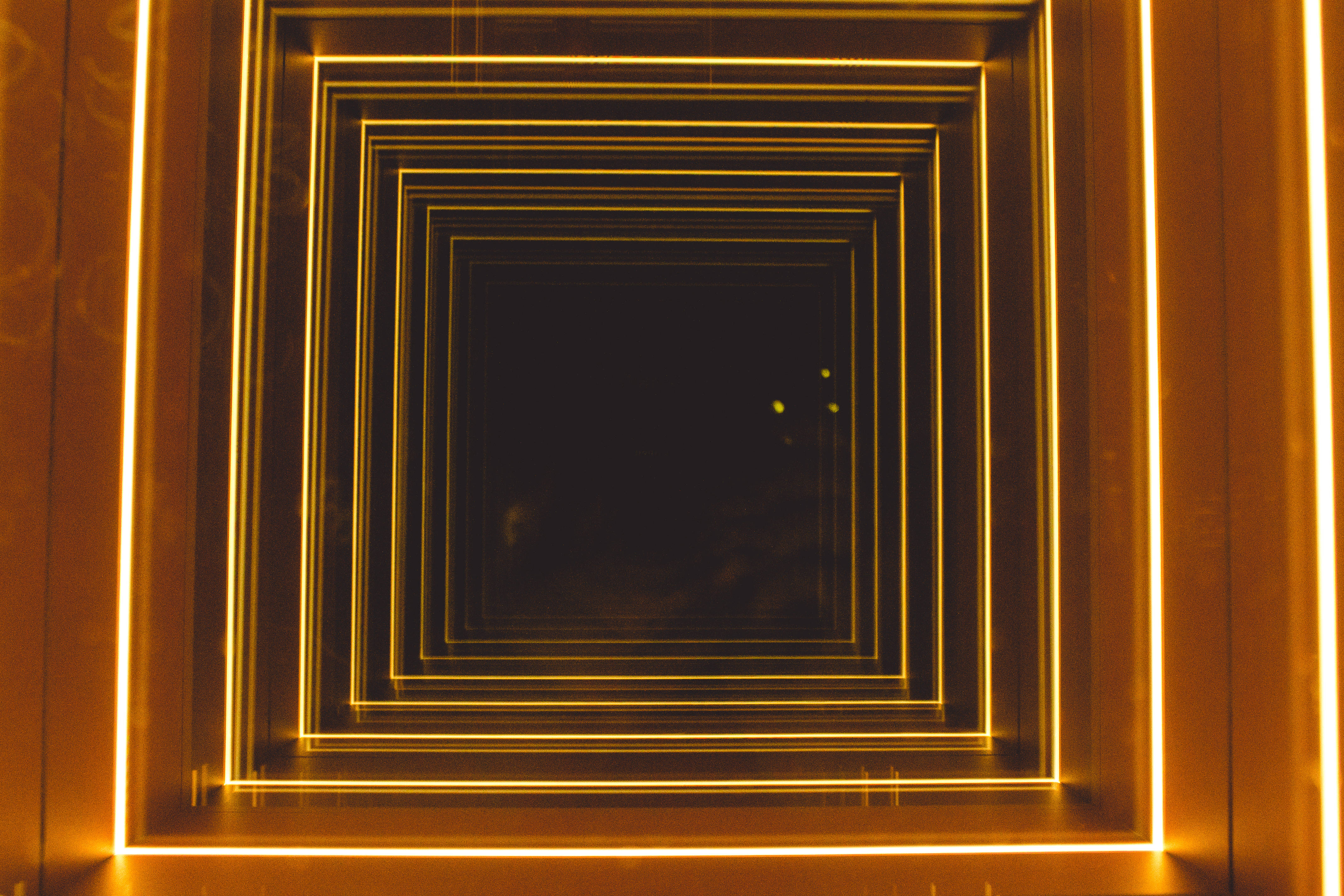 Illusion Yellow Lights Wallpaper — A mesmerizing tunnel of glowing golden neon squares receding into darkness with faint floating lights.