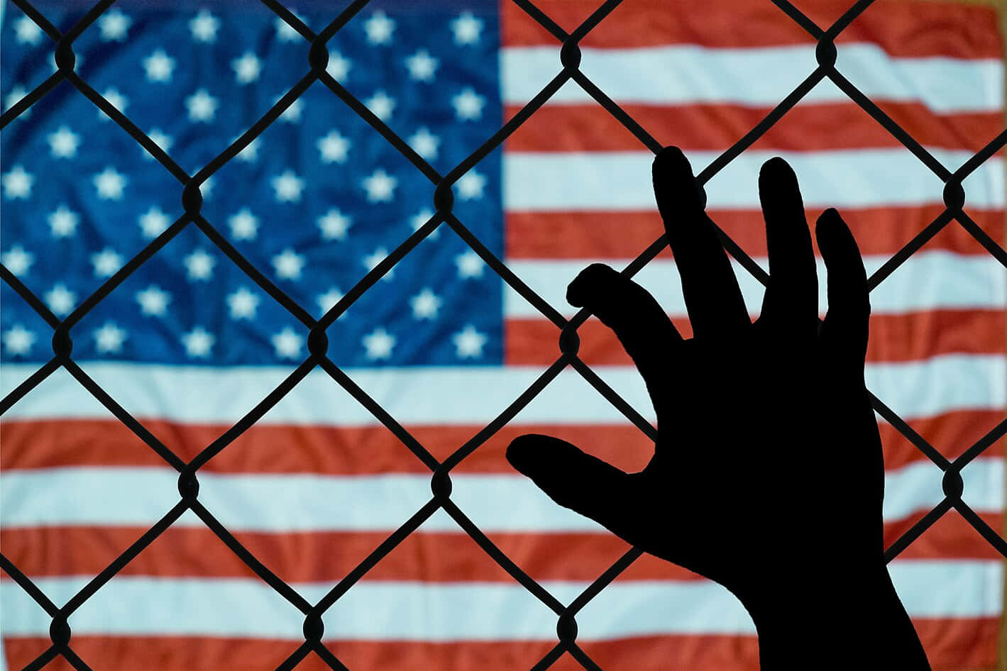 A Hand Reaching Out Of A Chain Link Fence