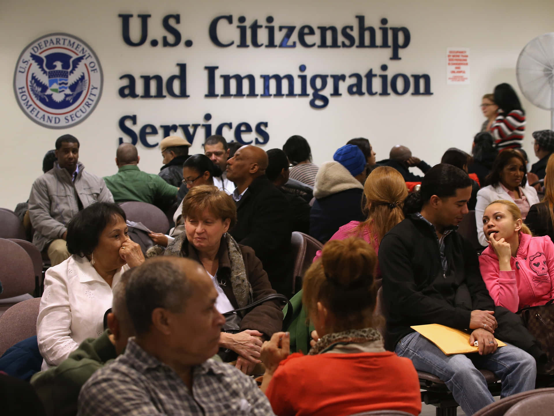 Ungruppo Di Persone Sedute In Una Stanza Con Un Cartello Che Dice Servizi Per La Cittadinanza E L'immigrazione Degli Stati Uniti.