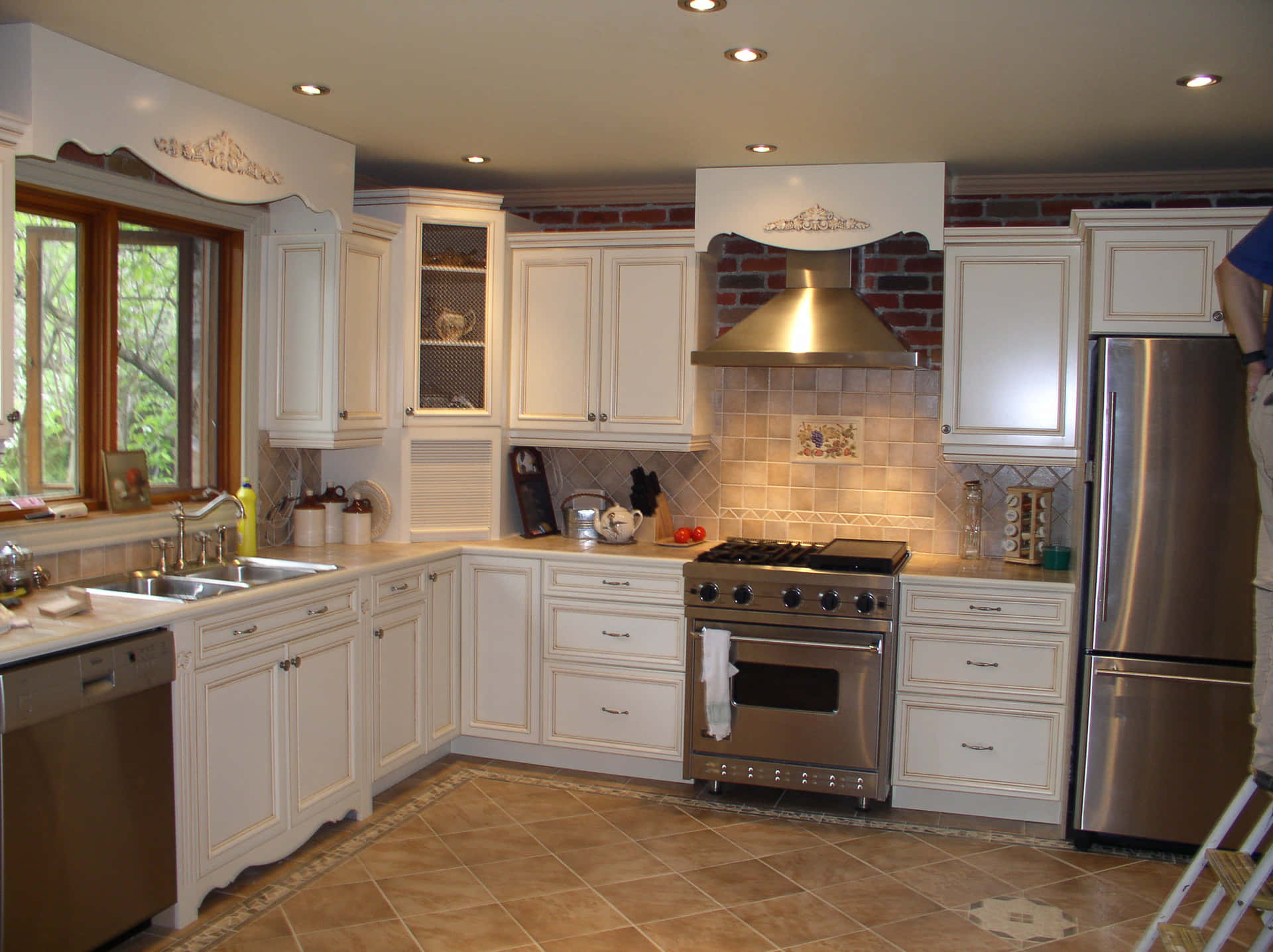 Incredible Kitchen Cabinetry Picture — A bright modern kitchen with white cabinets stainless steel appliances and a tiled floor bathed in natural light from a window.